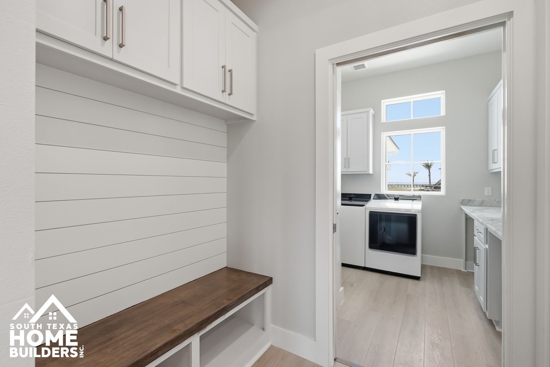 Bright white laundry room with built-in cabinets, wood countertop, and a view into a small kitchen.
