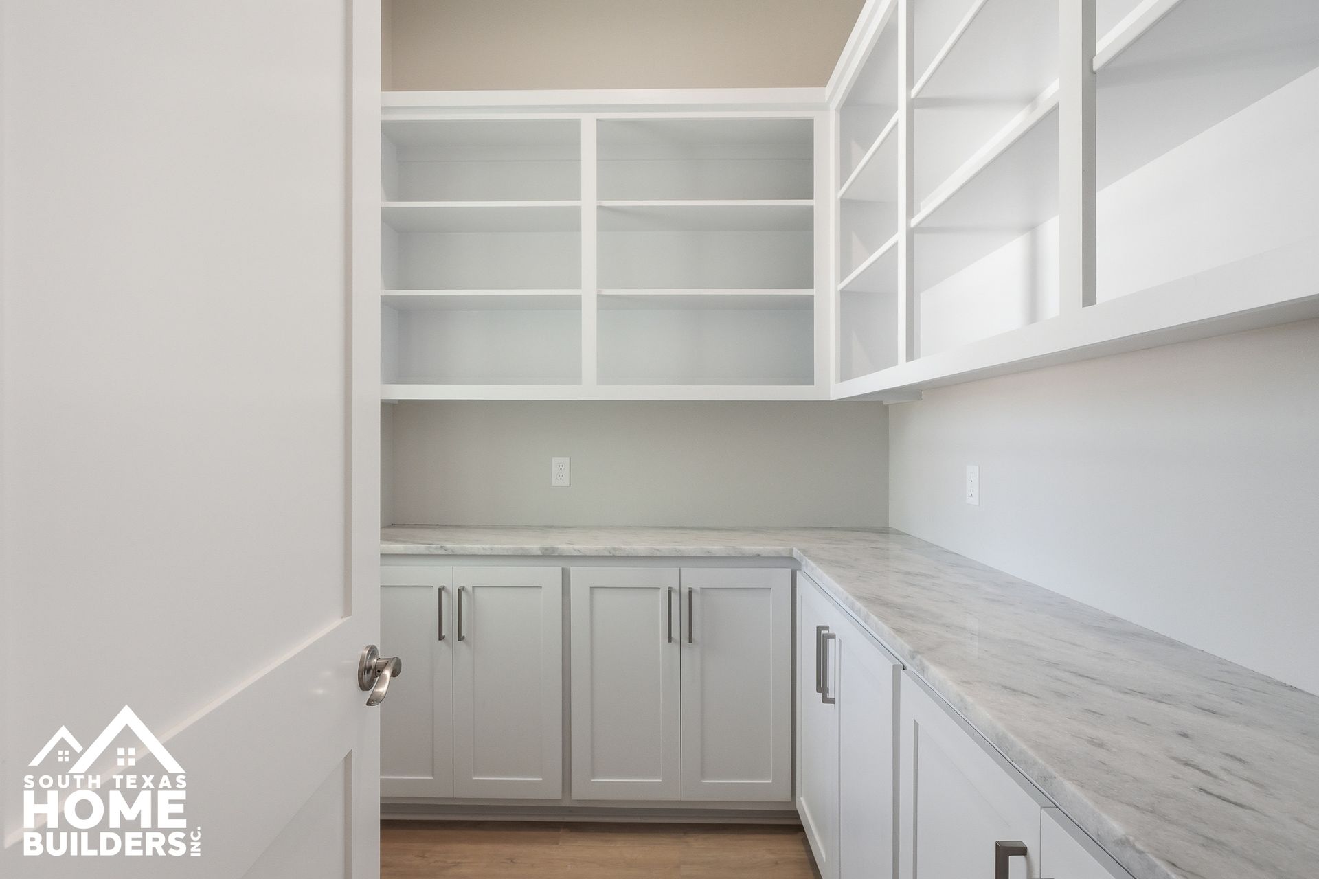 Bright white walk-in pantry with open shelves, cabinets, and light wood flooring