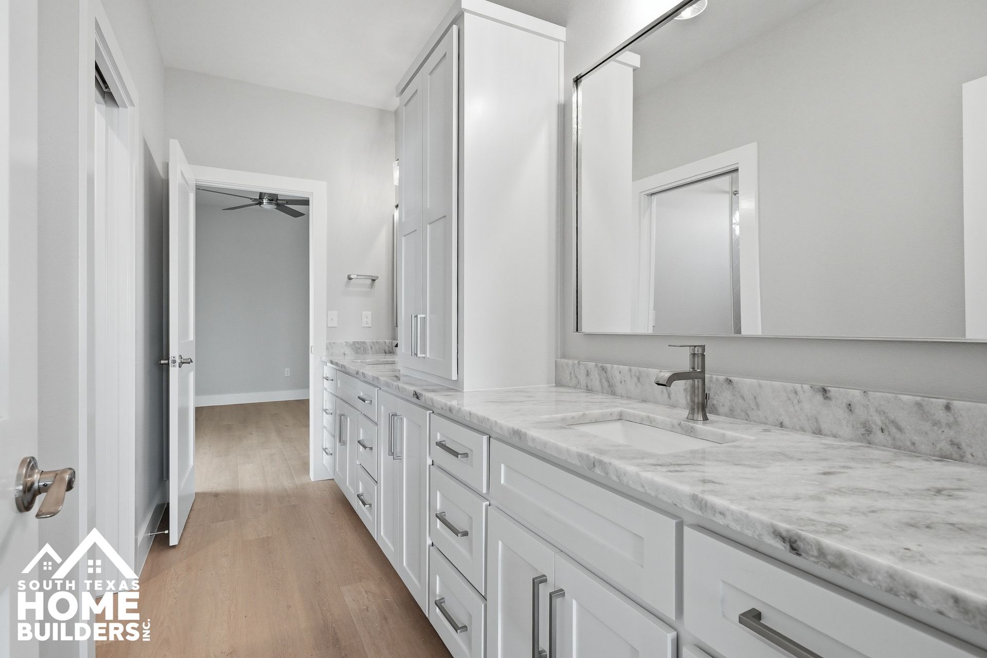 Bright white bathroom with double vanity, marble countertop, large mirror, and wood-look floor