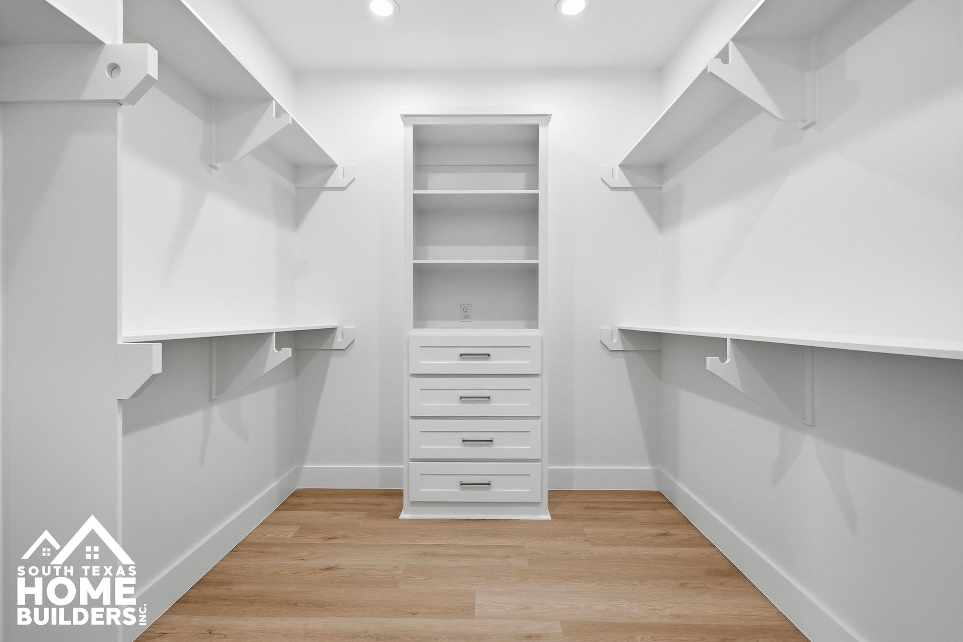Empty white walk-in closet with built-in shelves, drawers, and wood flooring