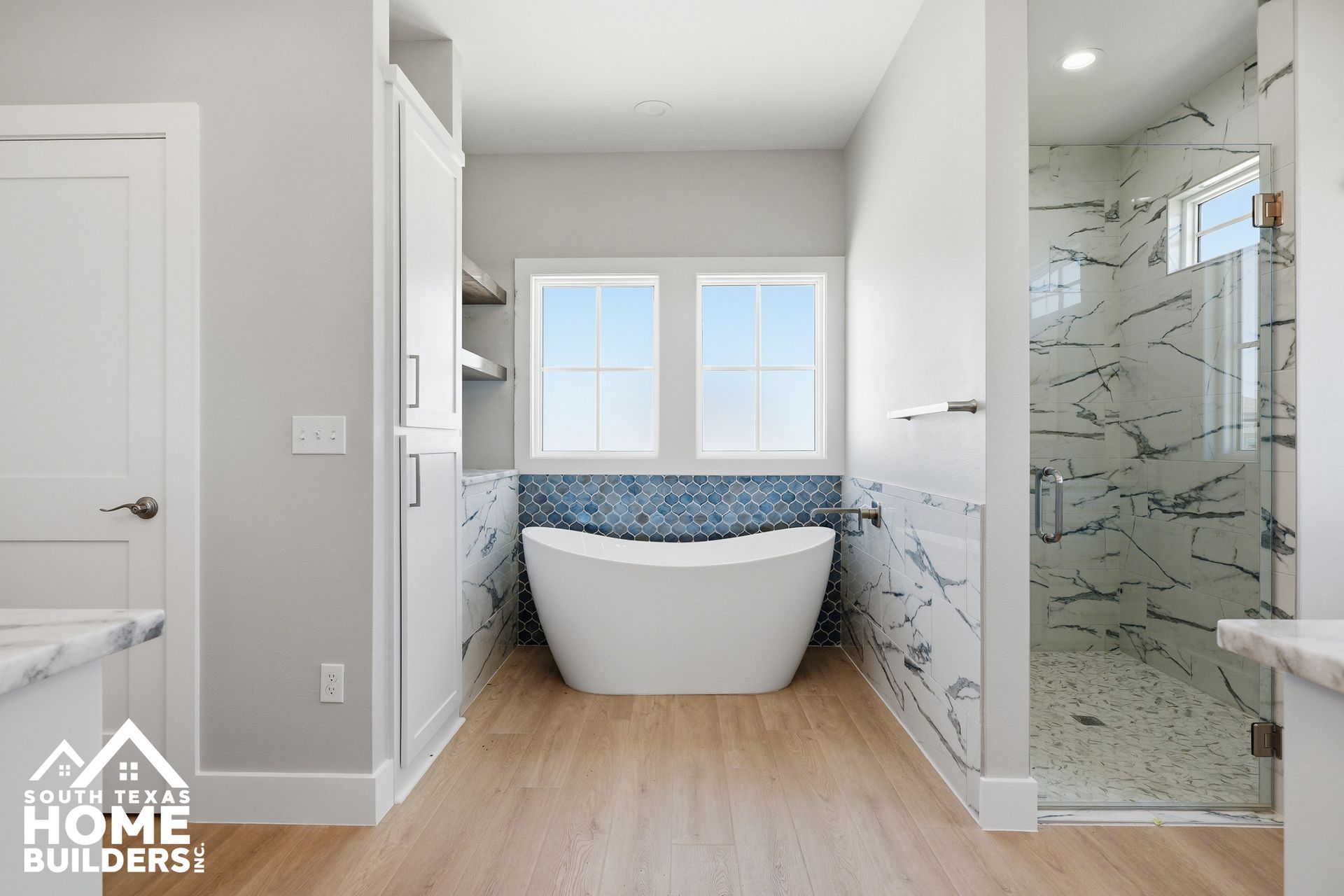 Modern bathroom with a freestanding tub, glass shower, and light wood flooring.