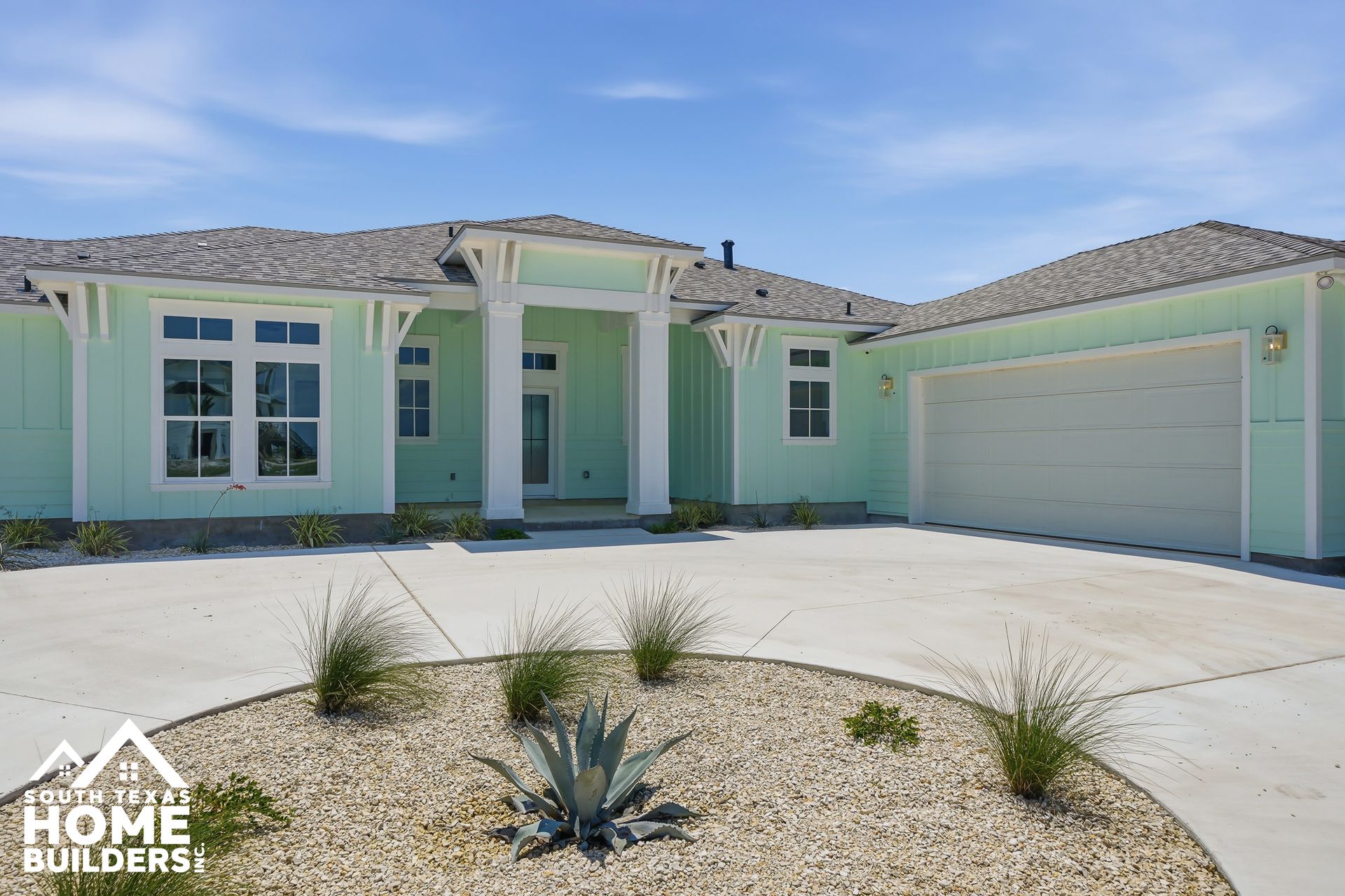 Mint green single-story house with two-car garage, desert landscaping, and a pale concrete driveway