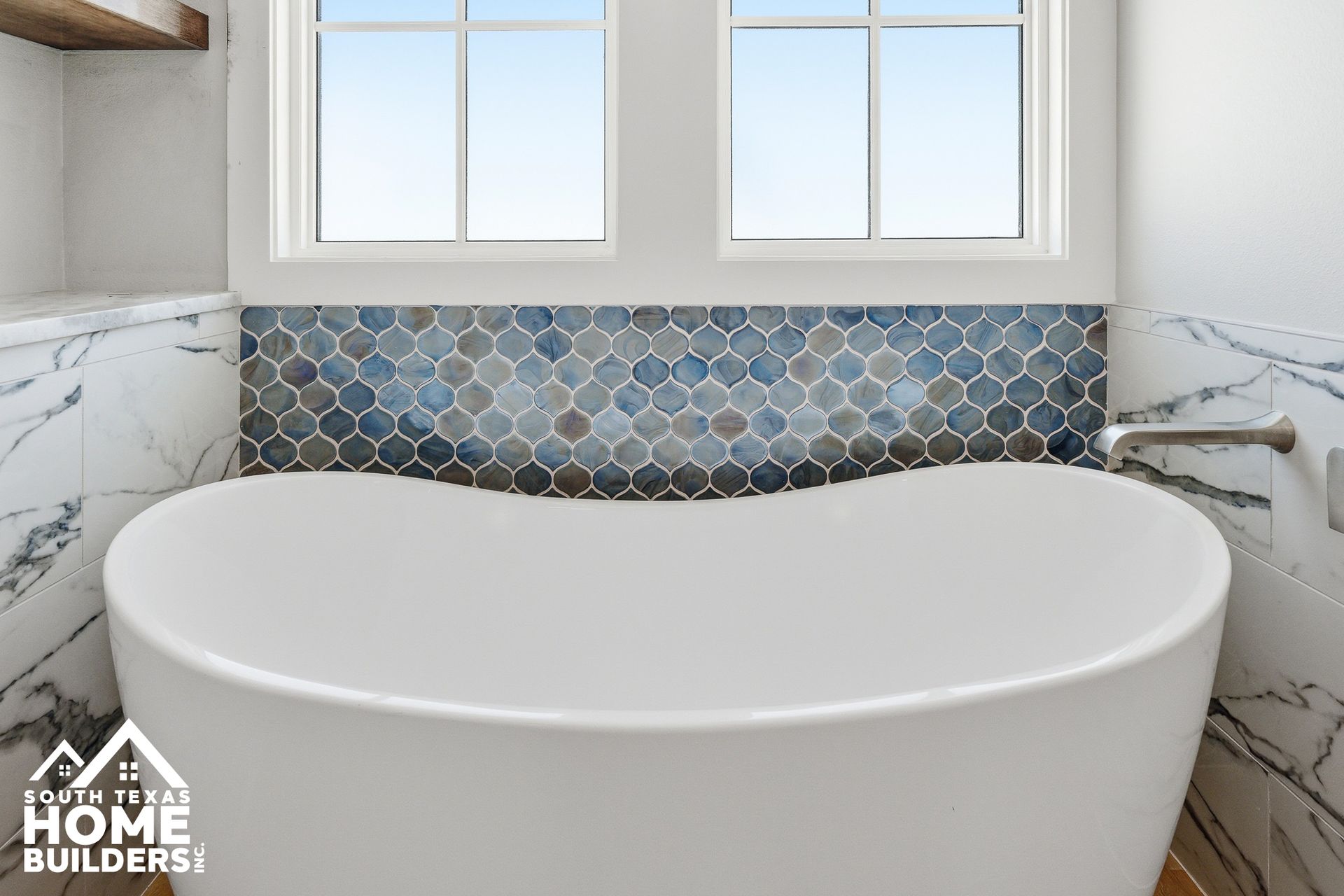 White freestanding bathtub in a bright bathroom with blue hex tile backsplash and marble walls