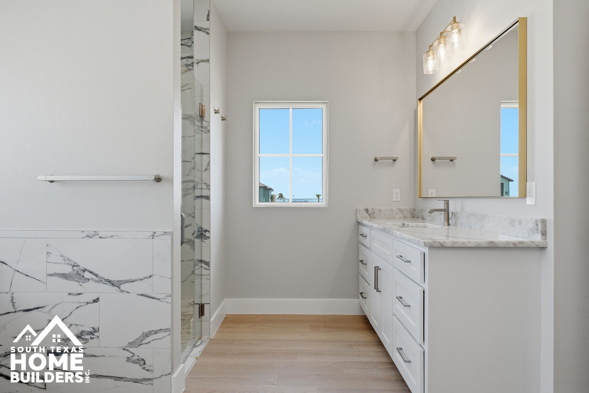 Bright modern bathroom with white marble vanity, large mirror, glass shower, and window for natural light
