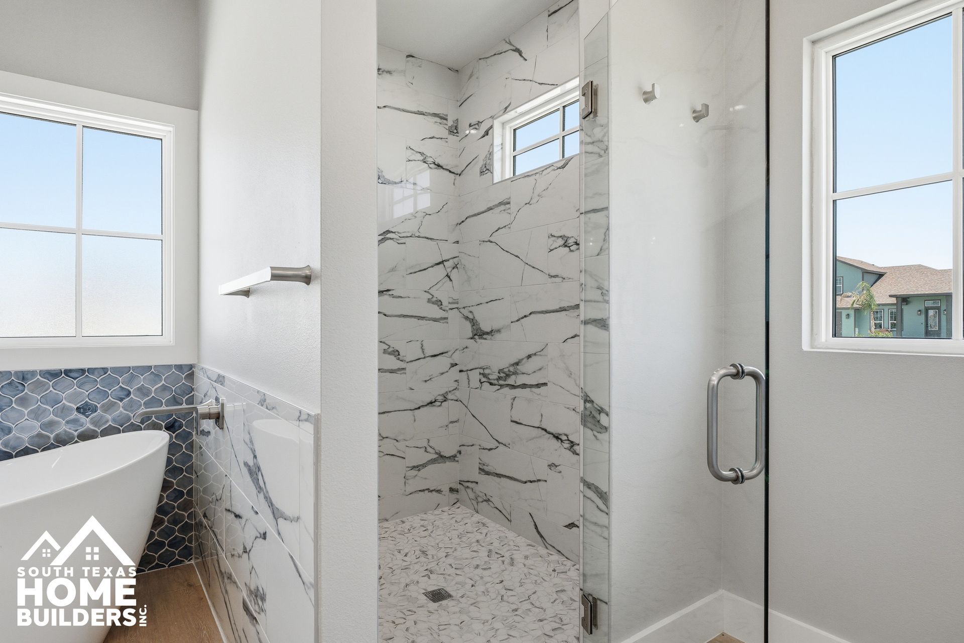Bright modern bathroom with a marble-tiled walk-in shower, white walls, and two windows