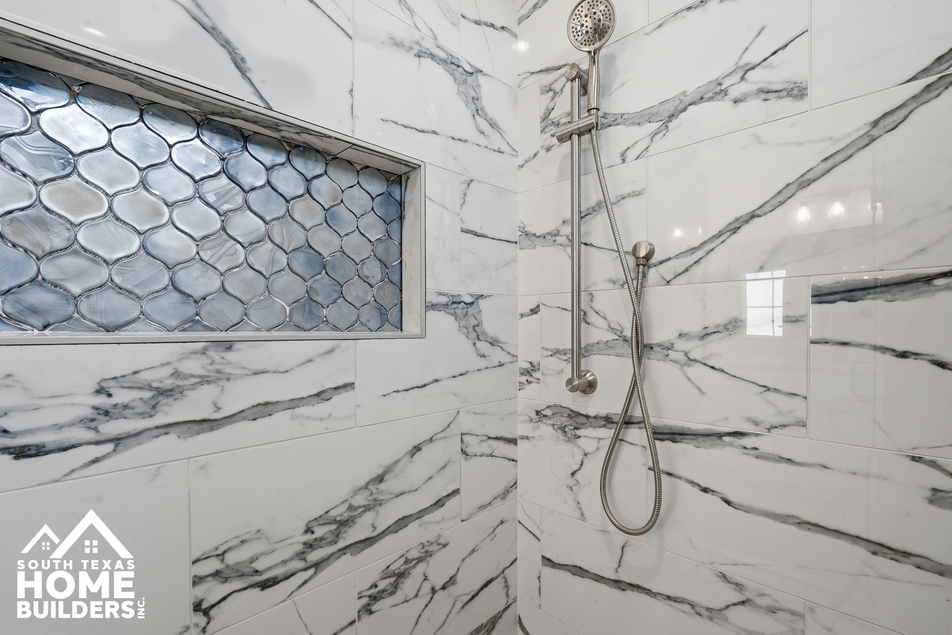 Luxury shower with white marble-look tile, blue mosaic window, and handheld showerhead