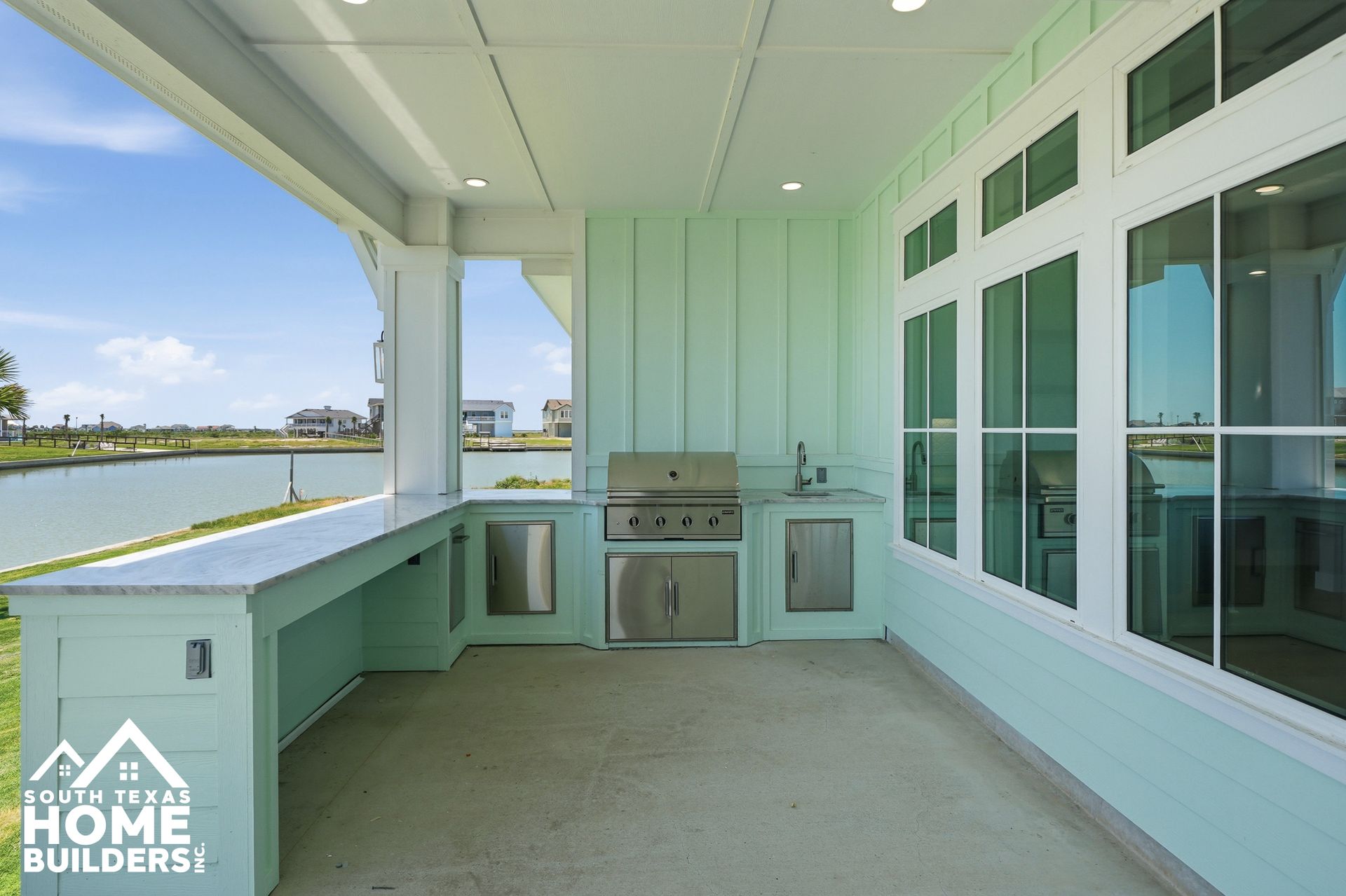 Covered waterfront patio with mint green cabinets, built-in grill, and water view