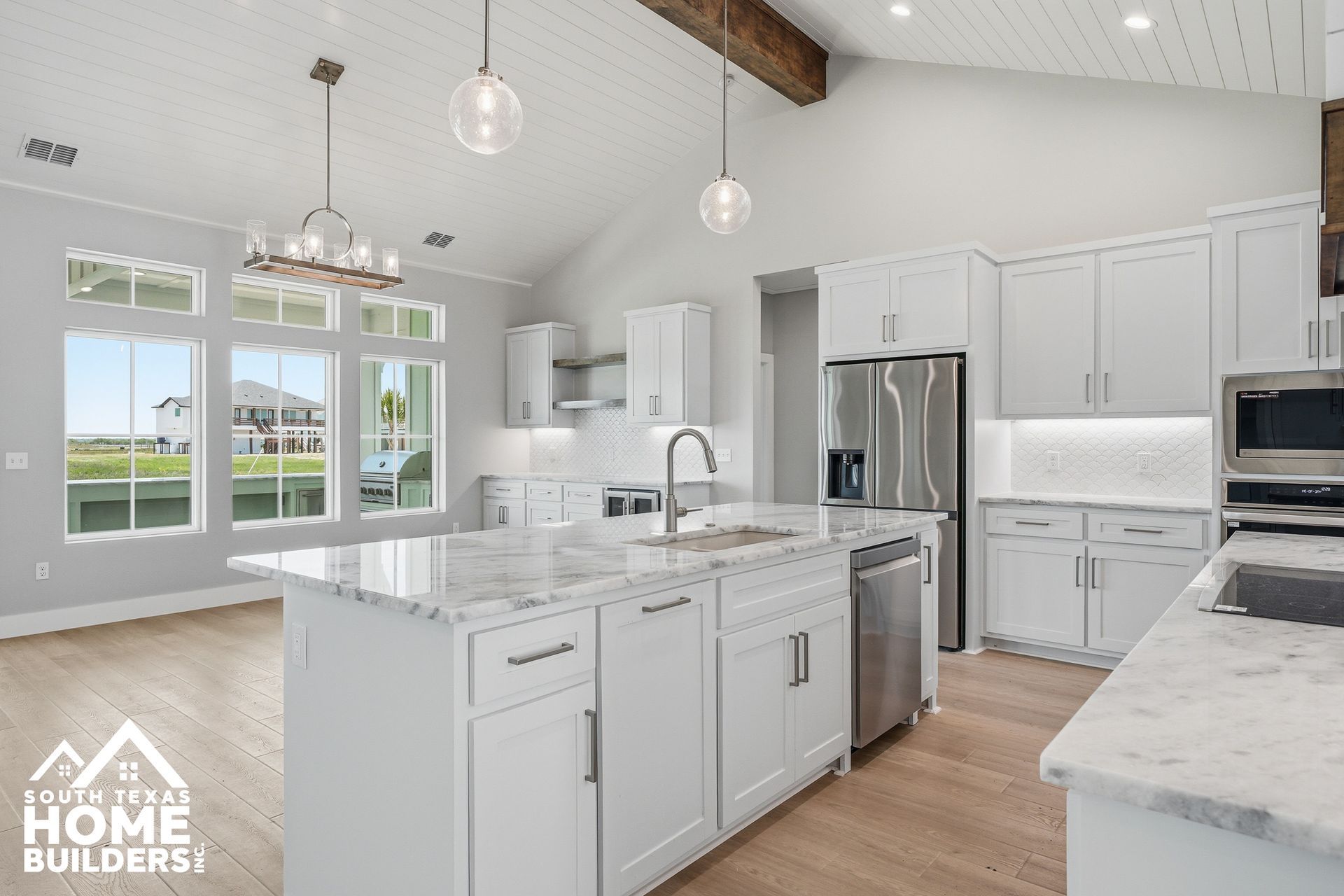 Bright white modern kitchen with island, stainless appliances, pendant lights, and large windows
