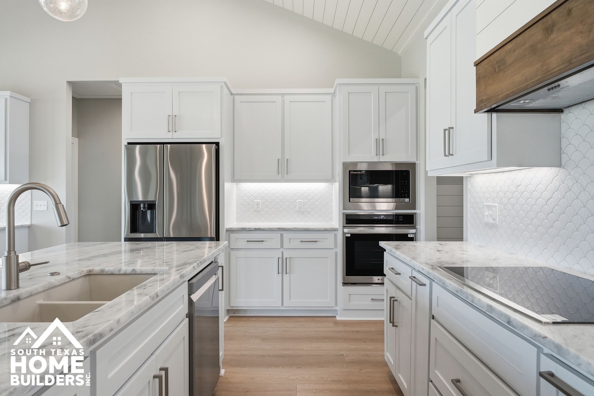Bright white modern kitchen with stainless steel appliances, island sink, and vaulted ceiling