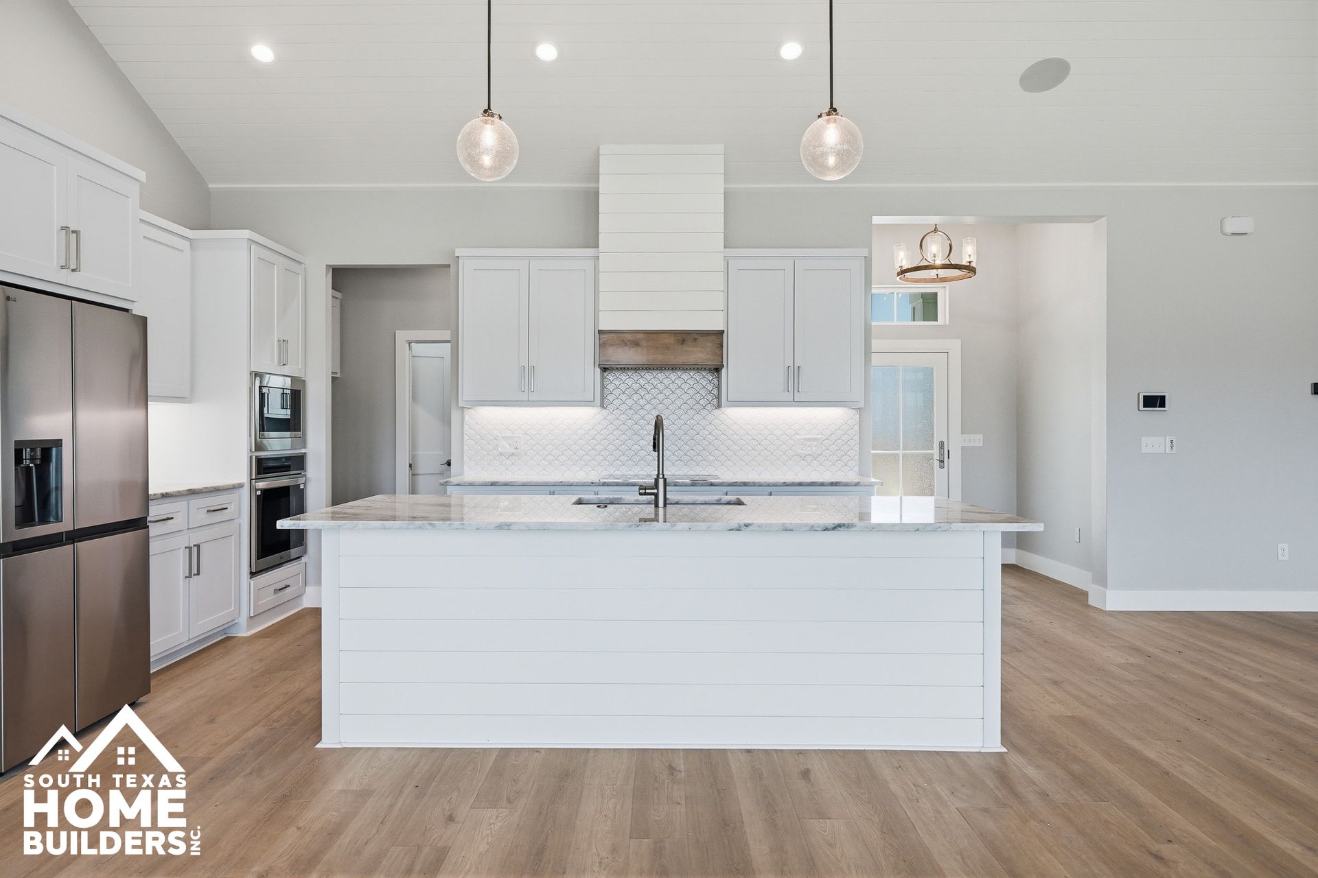 Bright white modern kitchen with island, stainless appliances, pendant lights, and wood flooring