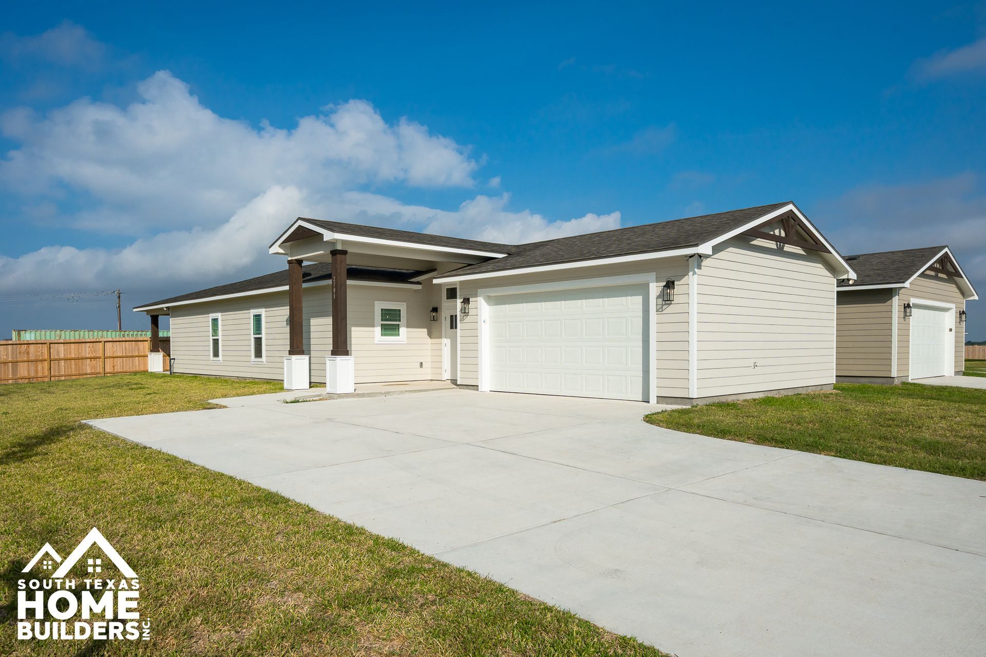 Light beige house with a two-car garage, concrete driveway, and grassy yard under a blue sky.
