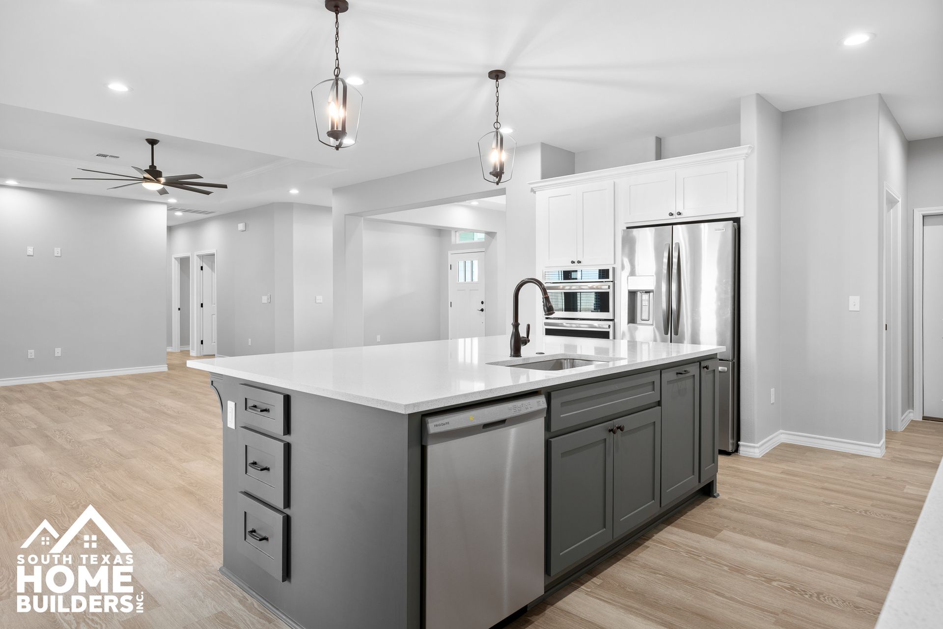 Modern kitchen with gray island, white countertops, stainless steel appliances, and wood-look flooring.