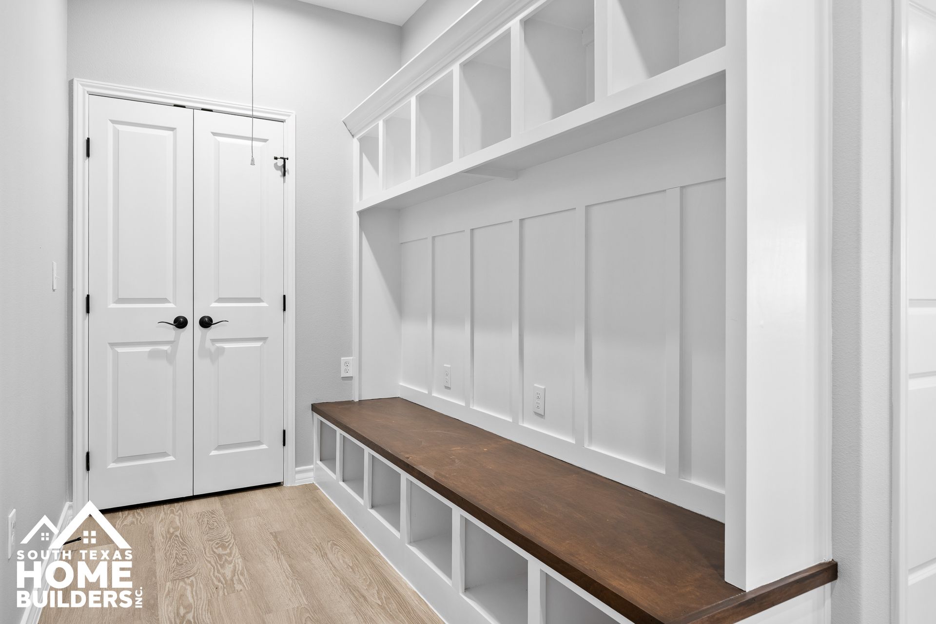 White built-in storage bench with open cubbies, shelves, and a dark wood bench seat in a hallway with a white door.