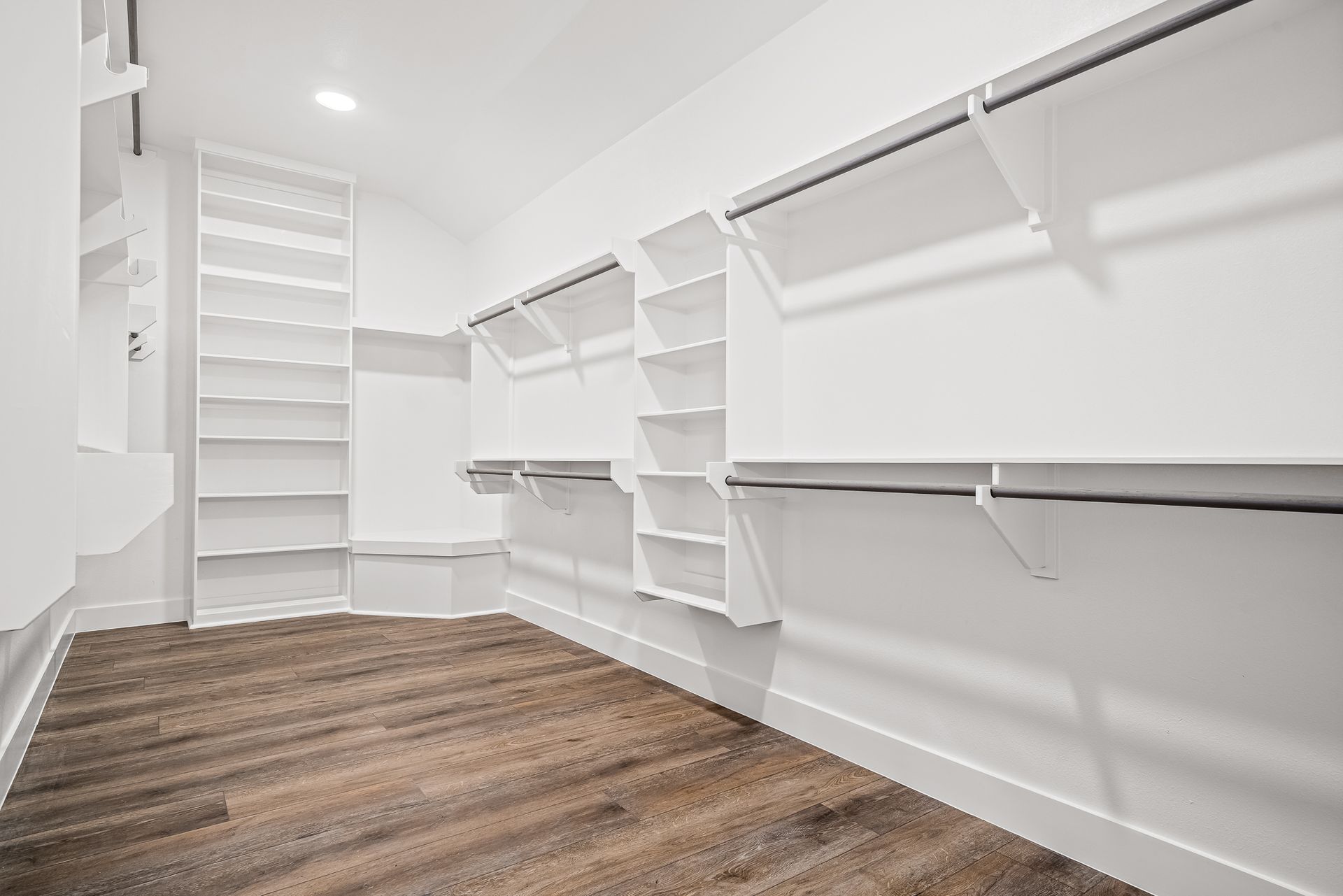 An empty walk in closet with wooden floors and white shelves.
