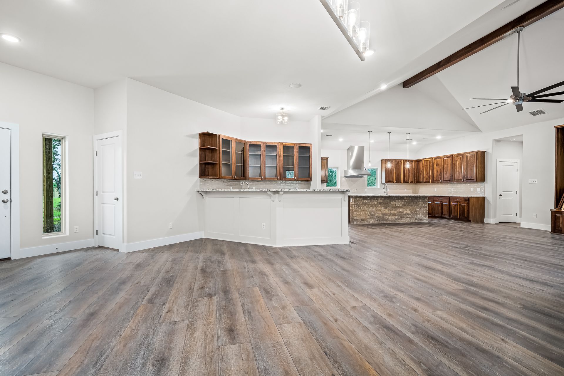 A large empty room with hardwood floors and a kitchen in the background.