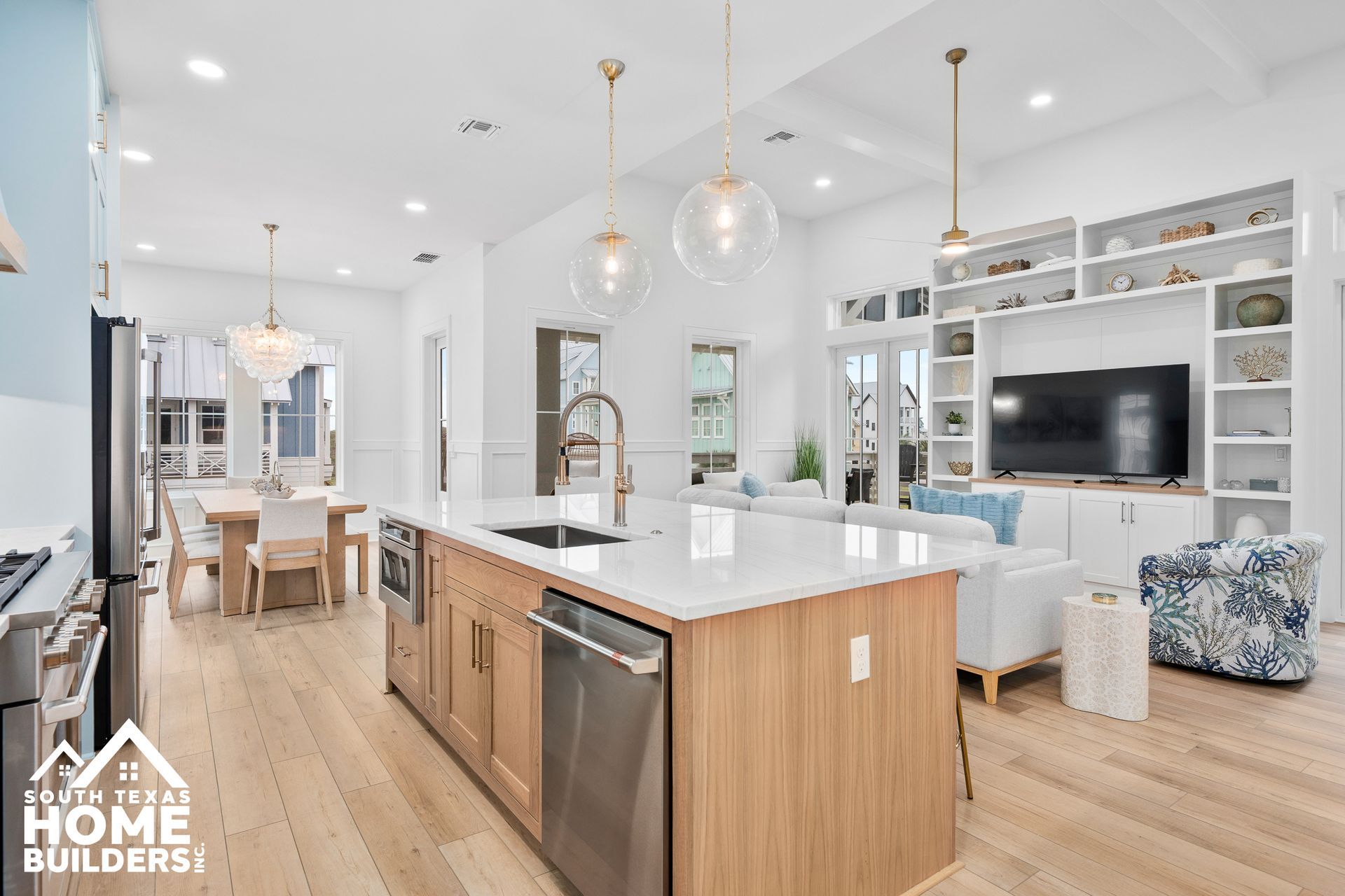 Modern kitchen and living room with light wood floors, white walls, and a large island.