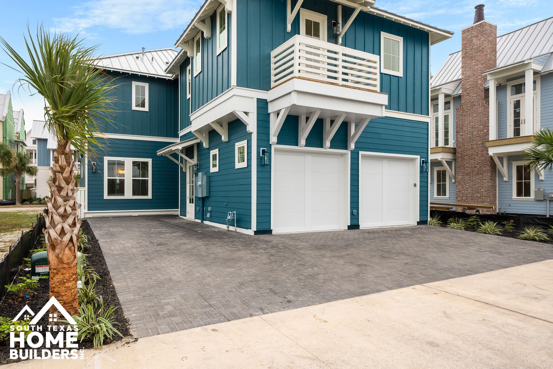 Blue house with white accents, two-car garage, and a balcony. Palm tree in front.