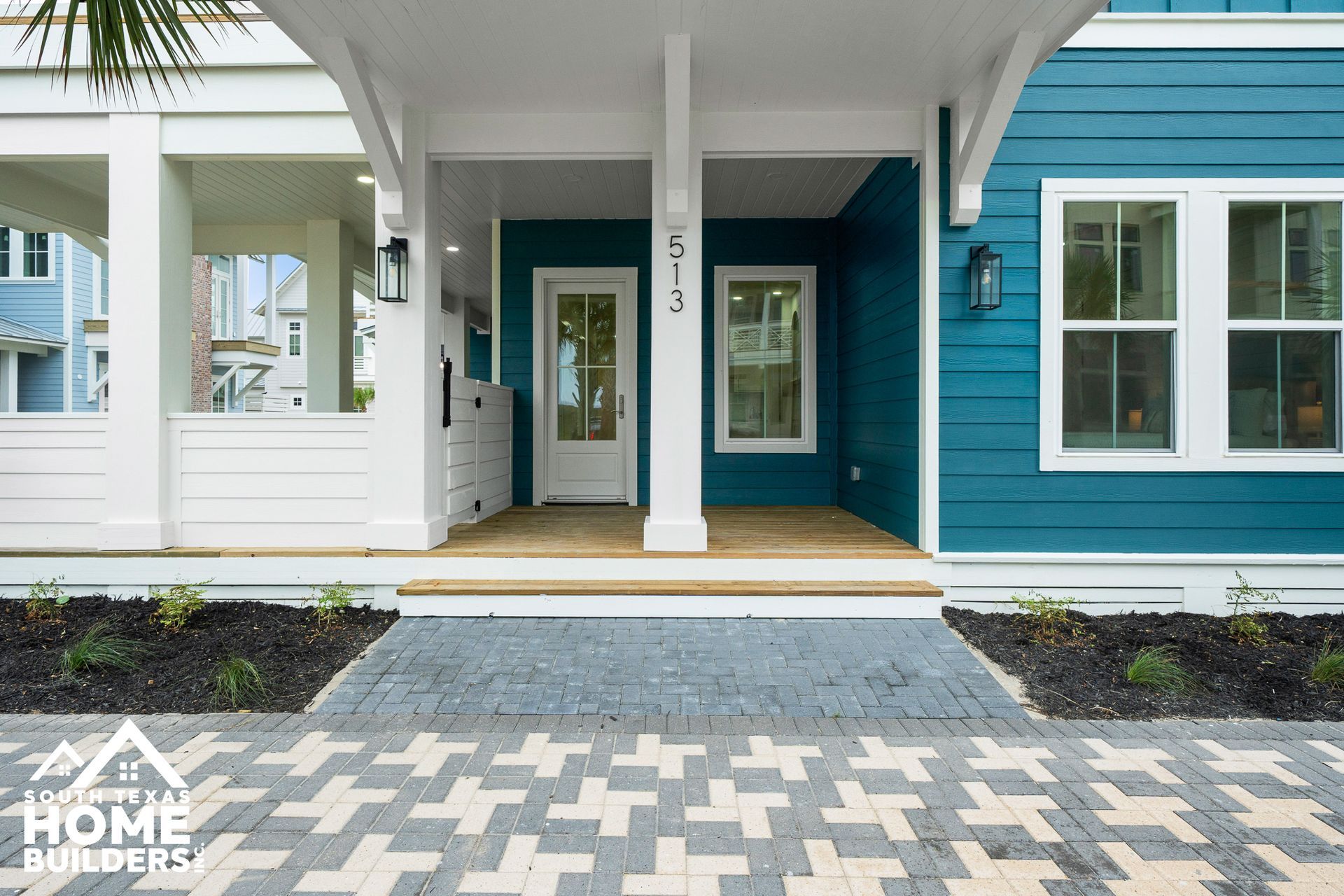 Teal and white house exterior with a covered porch and brick walkway.