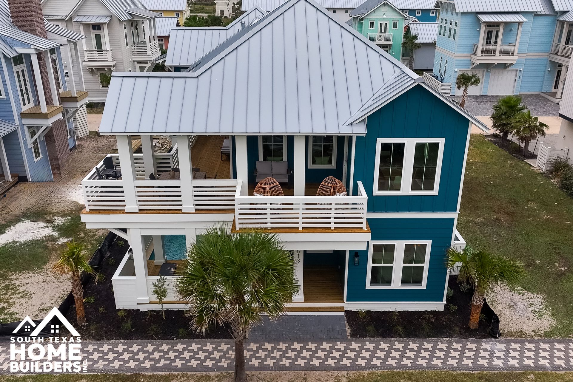 Two-story blue beach house with white trim, balconies, metal roof. Located in a coastal community with other similar homes.