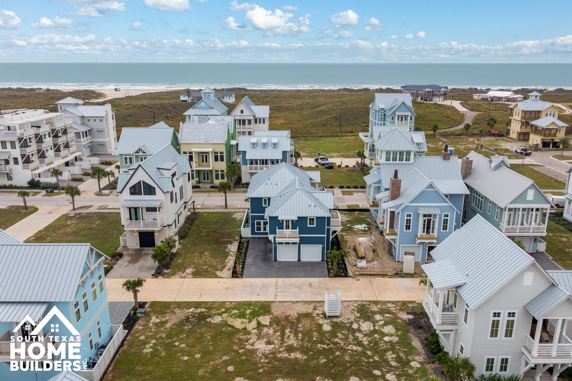 Aerial view of colorful beach houses with ocean and beach in the background under a blue sky.