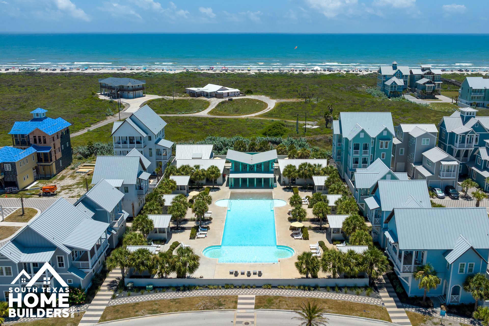 Aerial view of beachside houses, pool, and ocean on a sunny day.