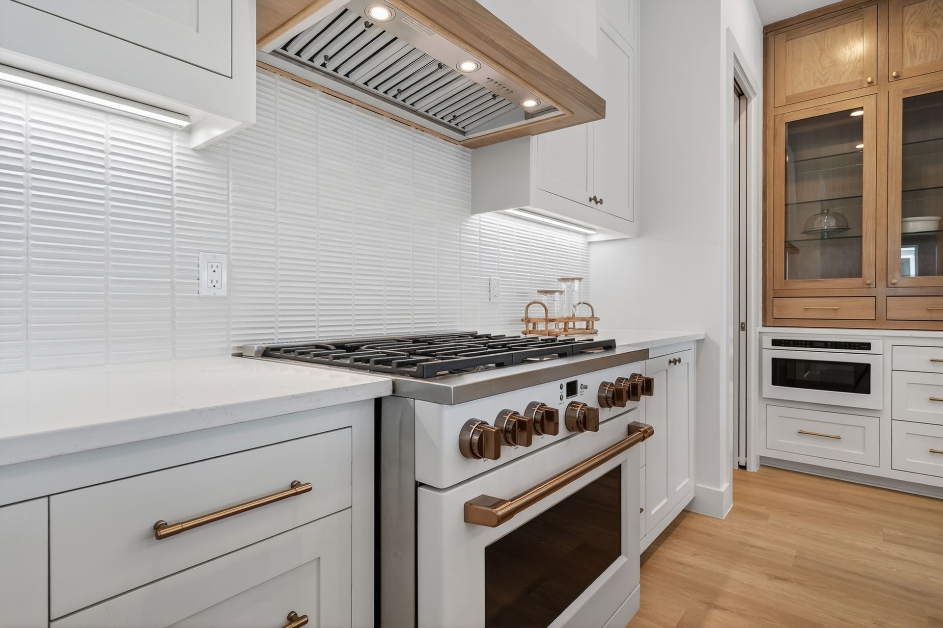 Bright white kitchen with gas range, brass accents, and wooden cabinets on the right