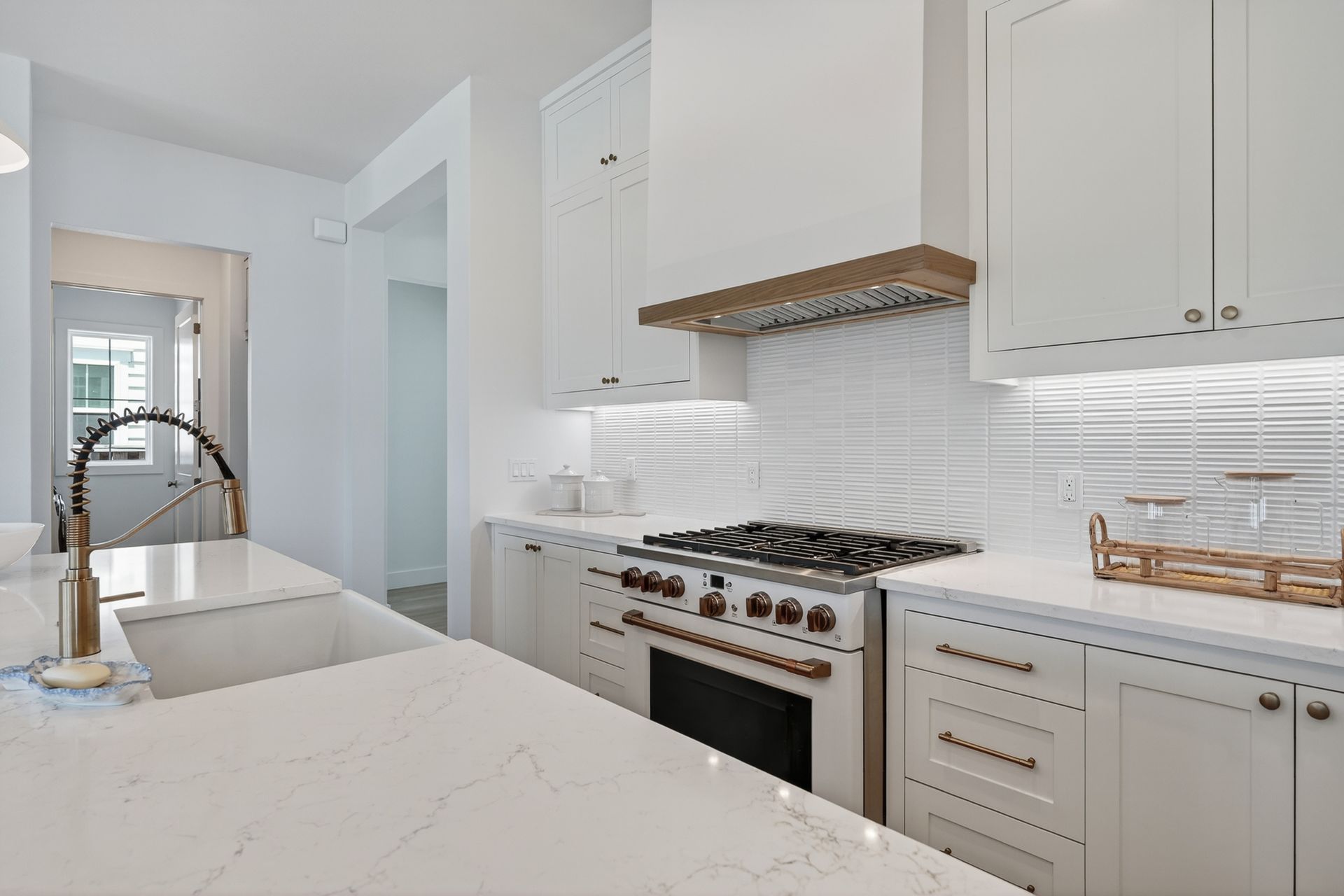 Bright white modern kitchen with marble counters, farmhouse sink, and stainless steel range under open shelving
