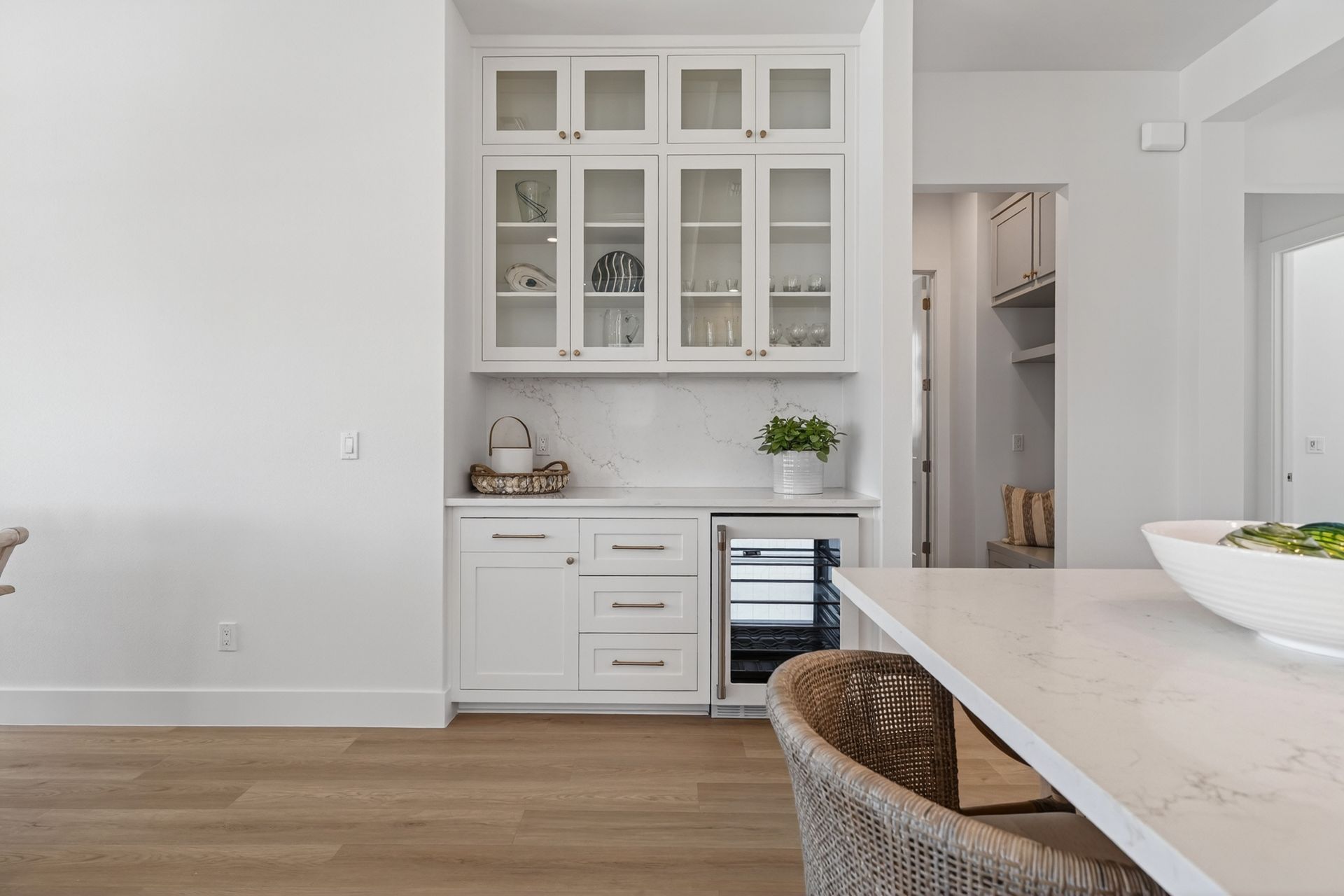 Bright modern kitchen with white cabinets, wood floors, and a marble island with wicker stool.