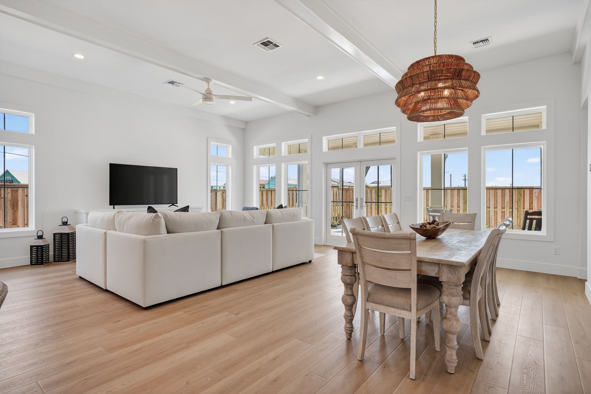 Bright open living-dining room with white sectional, wood floors, large windows, and woven pendant light