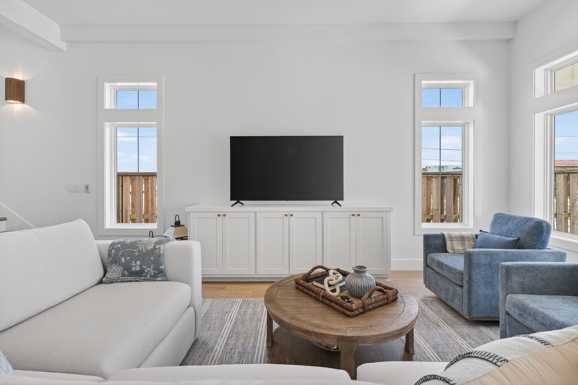Bright living room with white sofa, blue chair, wall-mounted TV, and a coffee table with decor.