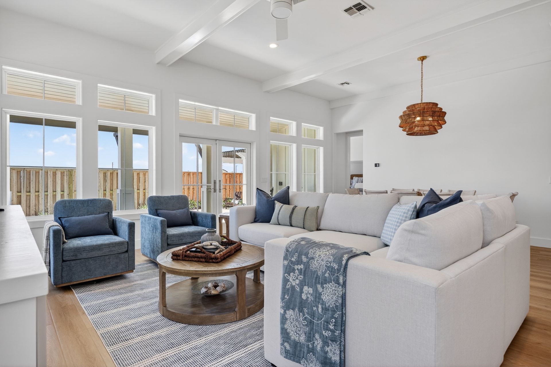 Bright living room with white sofa, blue chairs, coffee table, and large windows overlooking a deck