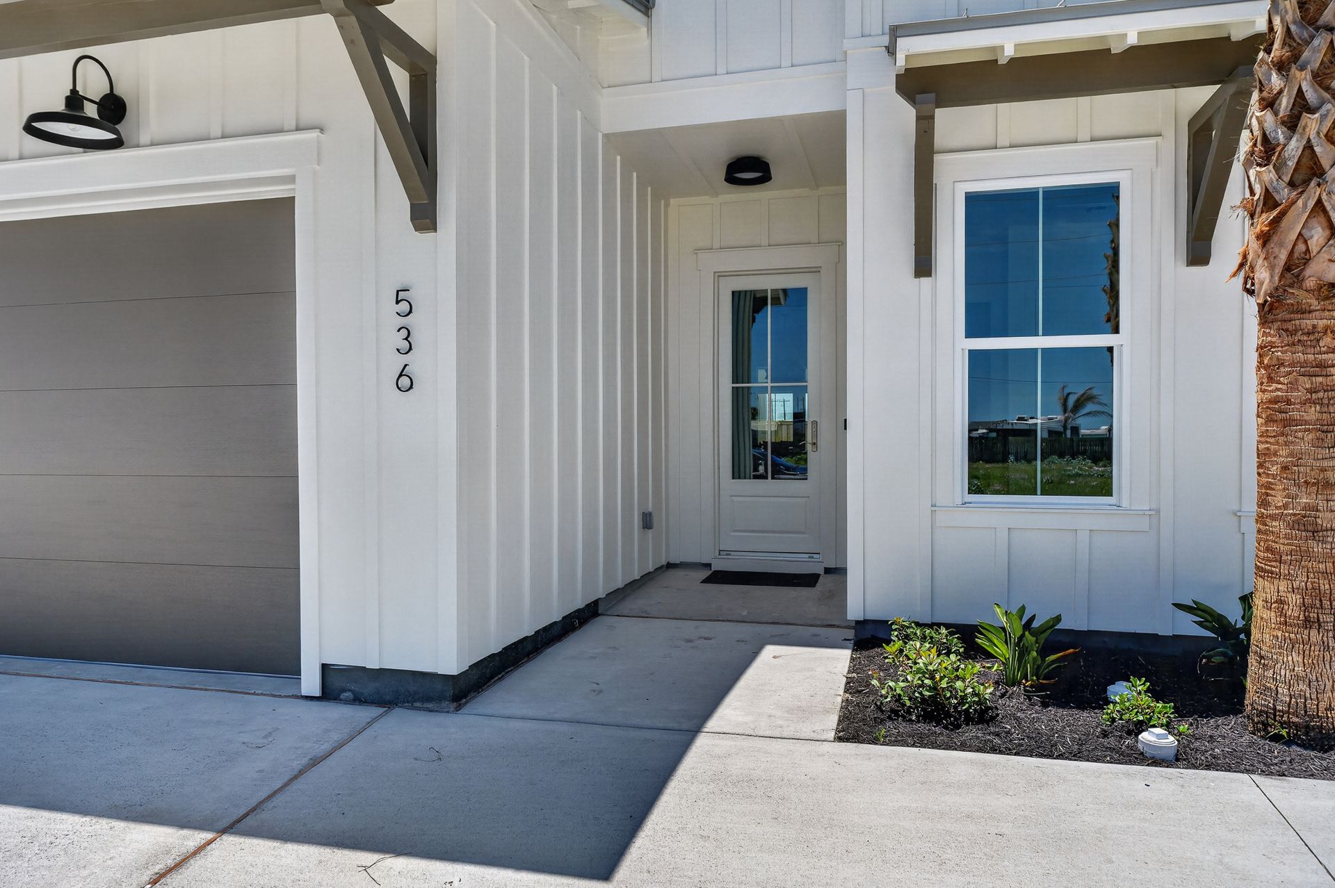 Front entrance of a white house with garage, front door, window, and small landscaped area