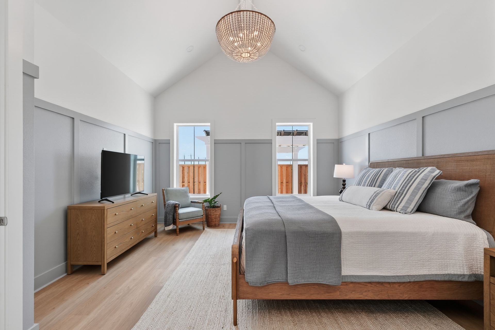 Bright bedroom with vaulted ceiling, bed, dresser, TV, and two windows with a city view