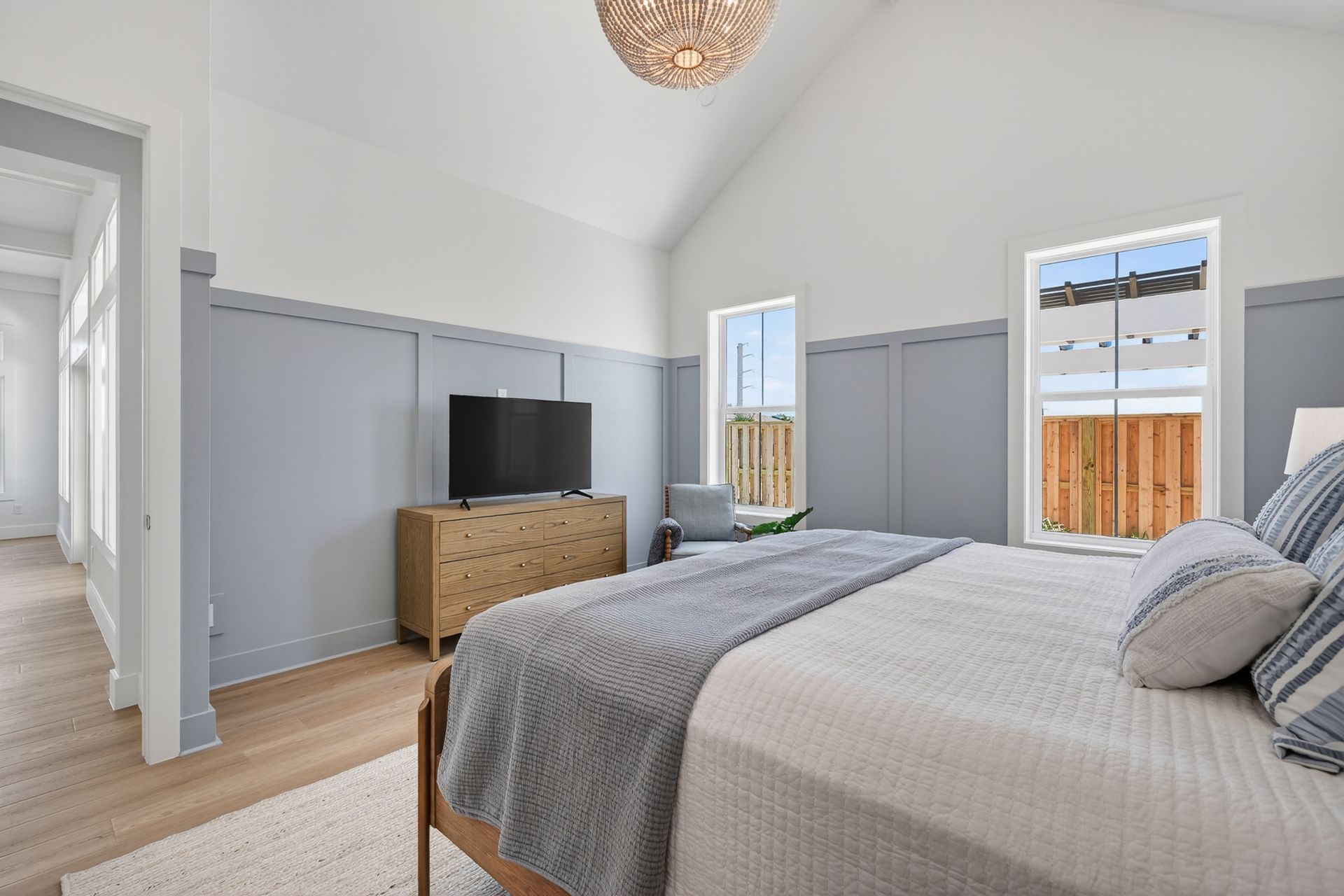 Bright bedroom with a bed, dresser and TV, gray closet doors, and windows looking out to a deck.