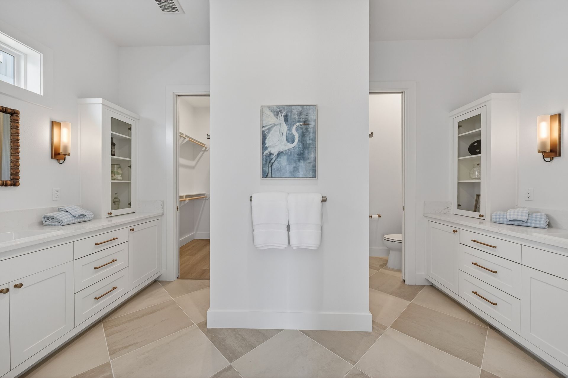 Bright white bathroom with dual vanities, central partition, and towel on a minimalist wall art display