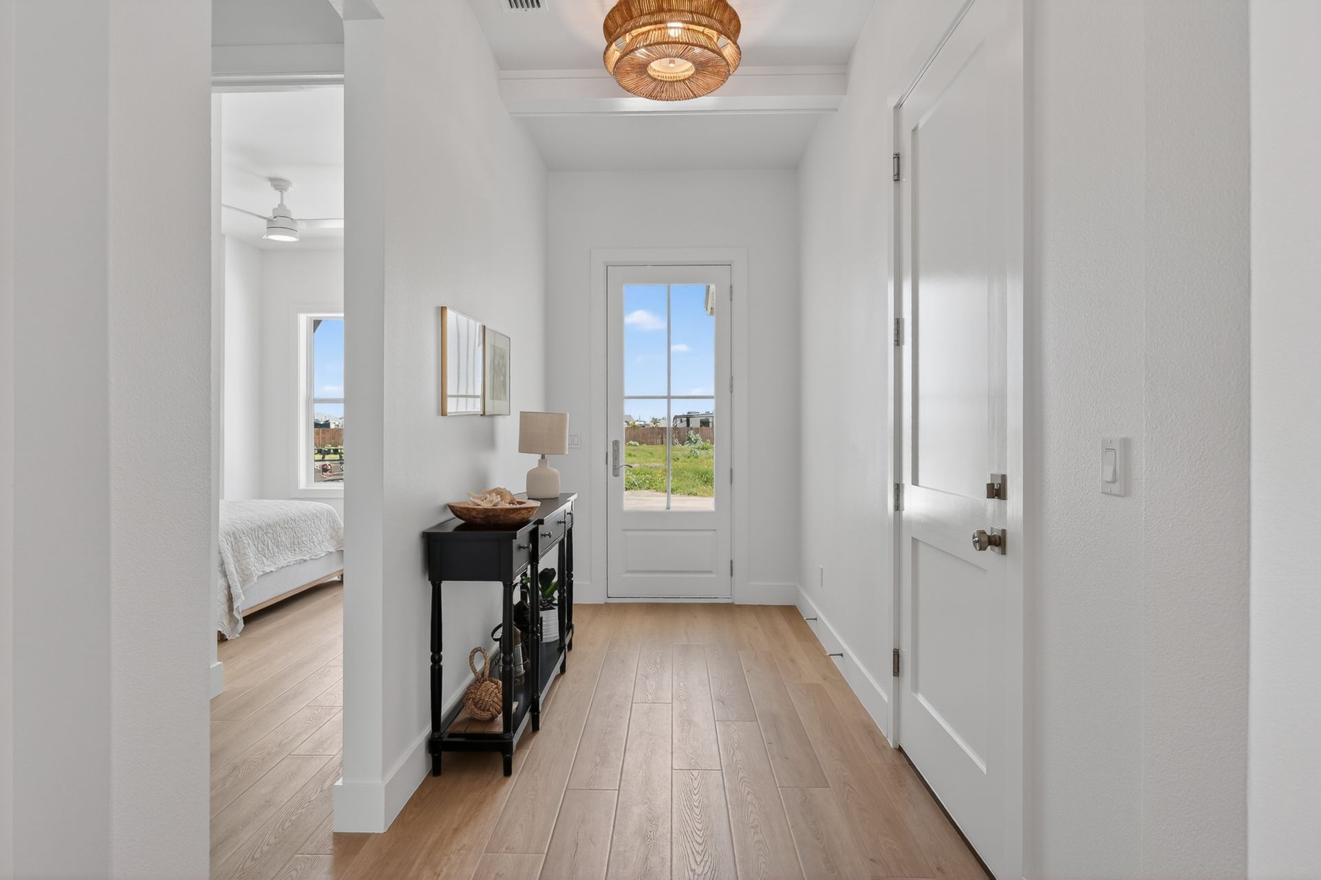 Bright hallway with light wood floors, white walls, a black console table, and a glass door at the end.