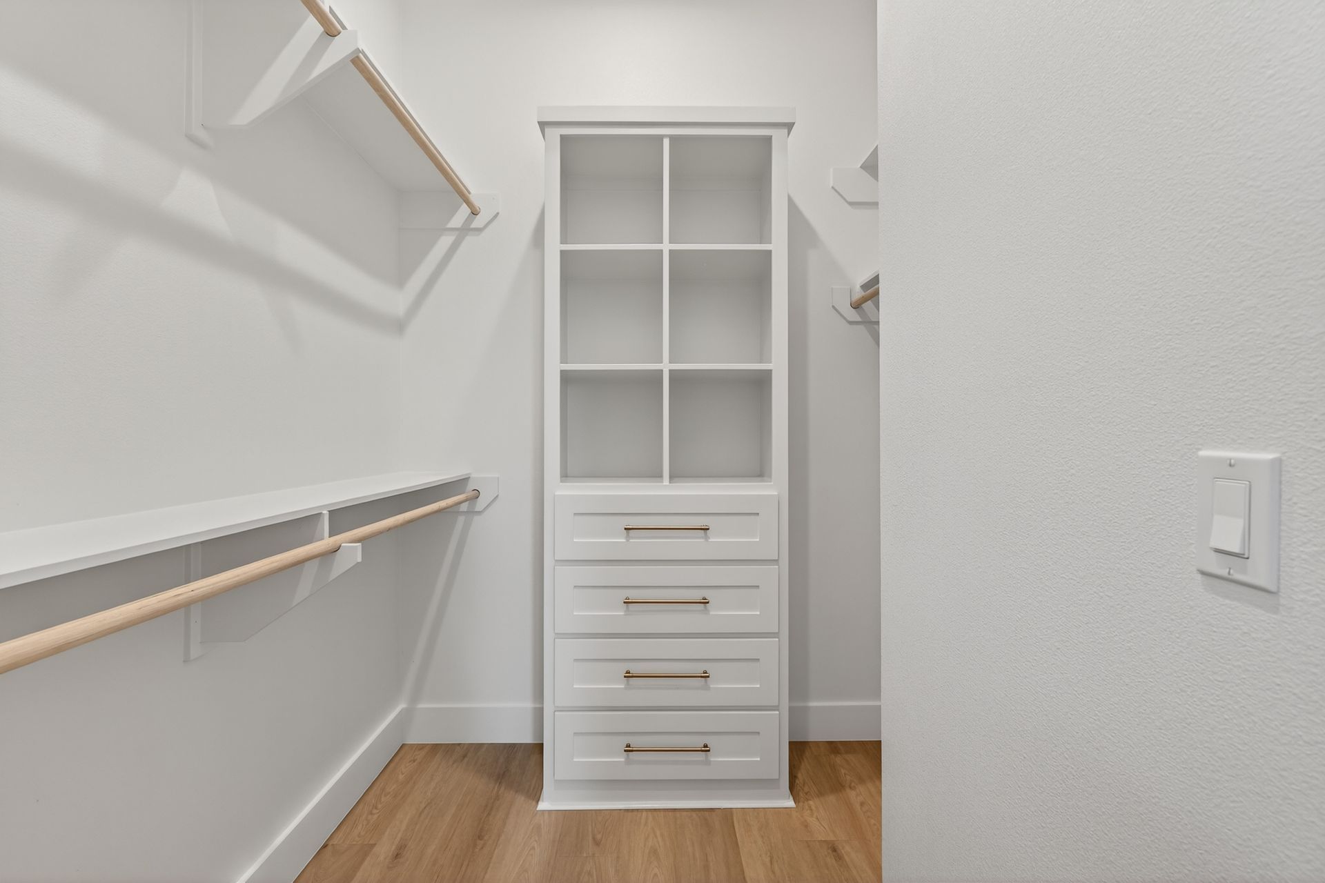 White walk-in closet with shelves, drawers, hanging rods, and wood flooring.