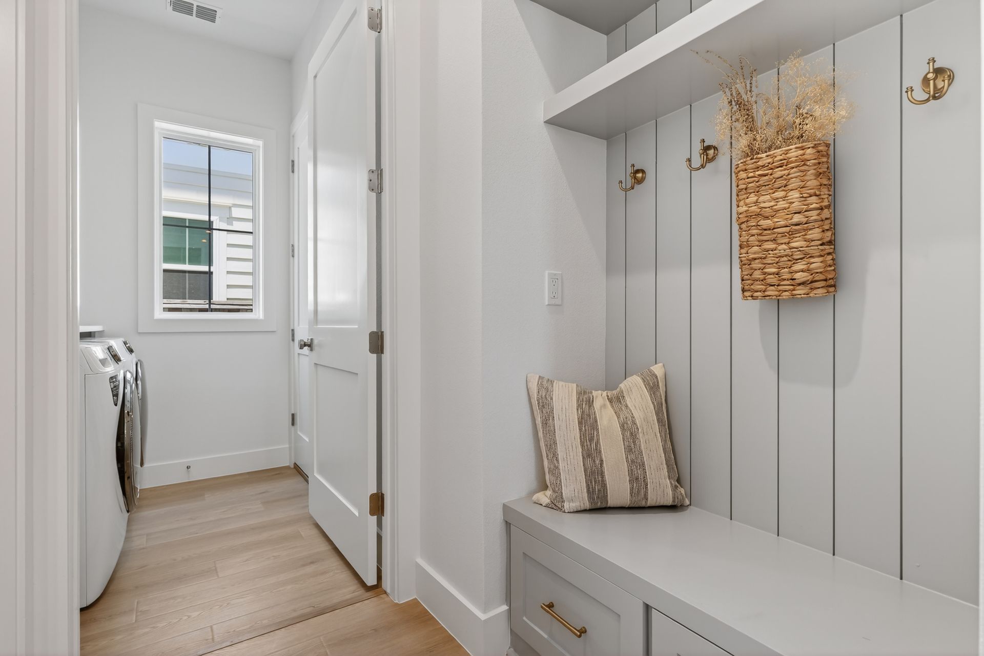Bright laundry room with white built-in bench, hooks, and a washer near a small window.