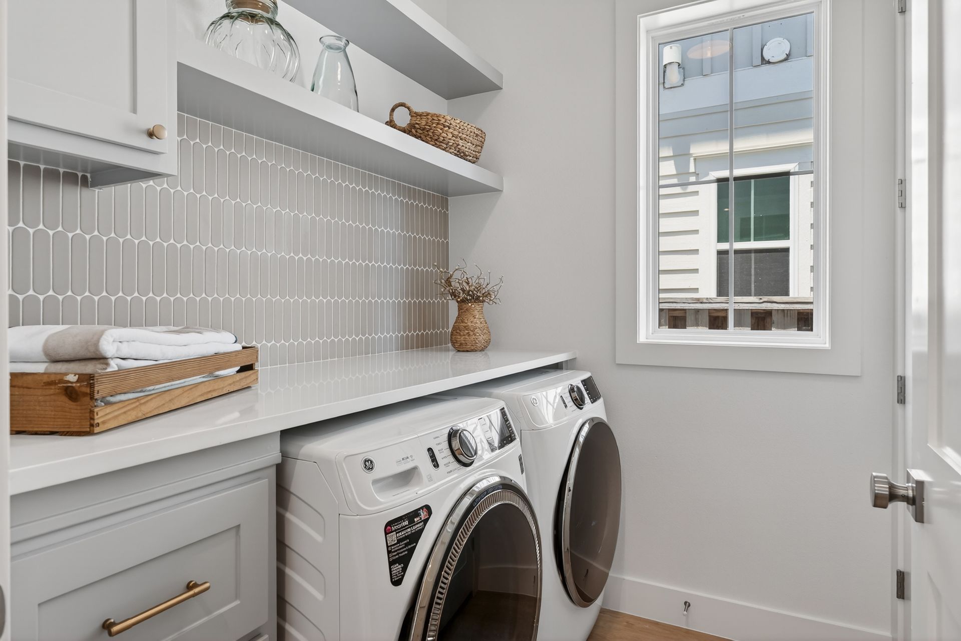 Bright laundry room with white washer and dryer, gray tile backsplash, and a windowed door.