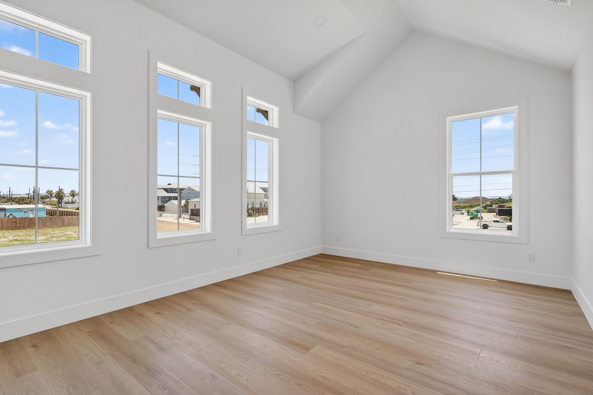 Empty bright room with white walls, light wood floors, and multiple tall windows.
