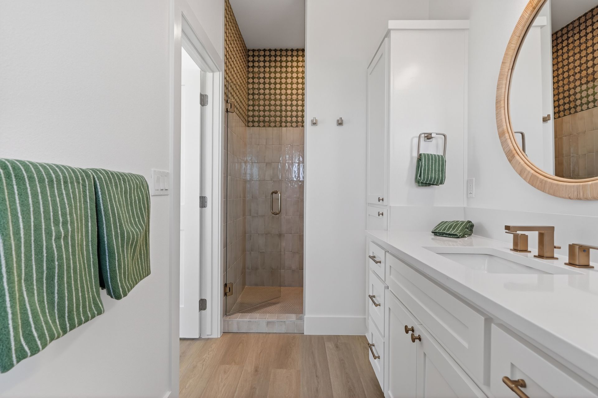 Bright bathroom with double vanity, round mirror, green towels, and tiled shower doorway.