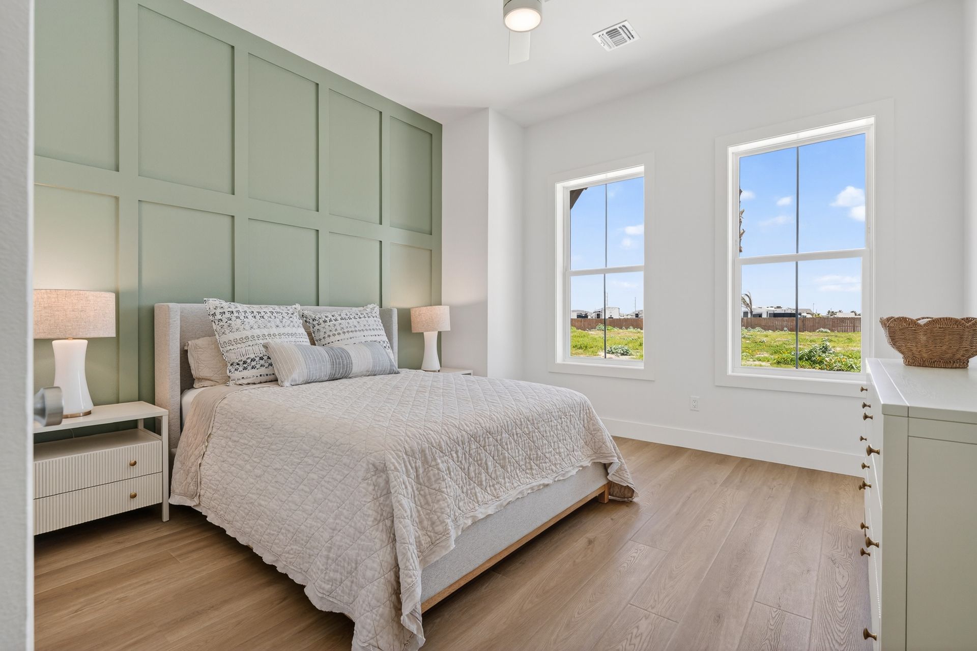 Bright bedroom with a green paneled accent wall, white bedding, and large windows overlooking a view.