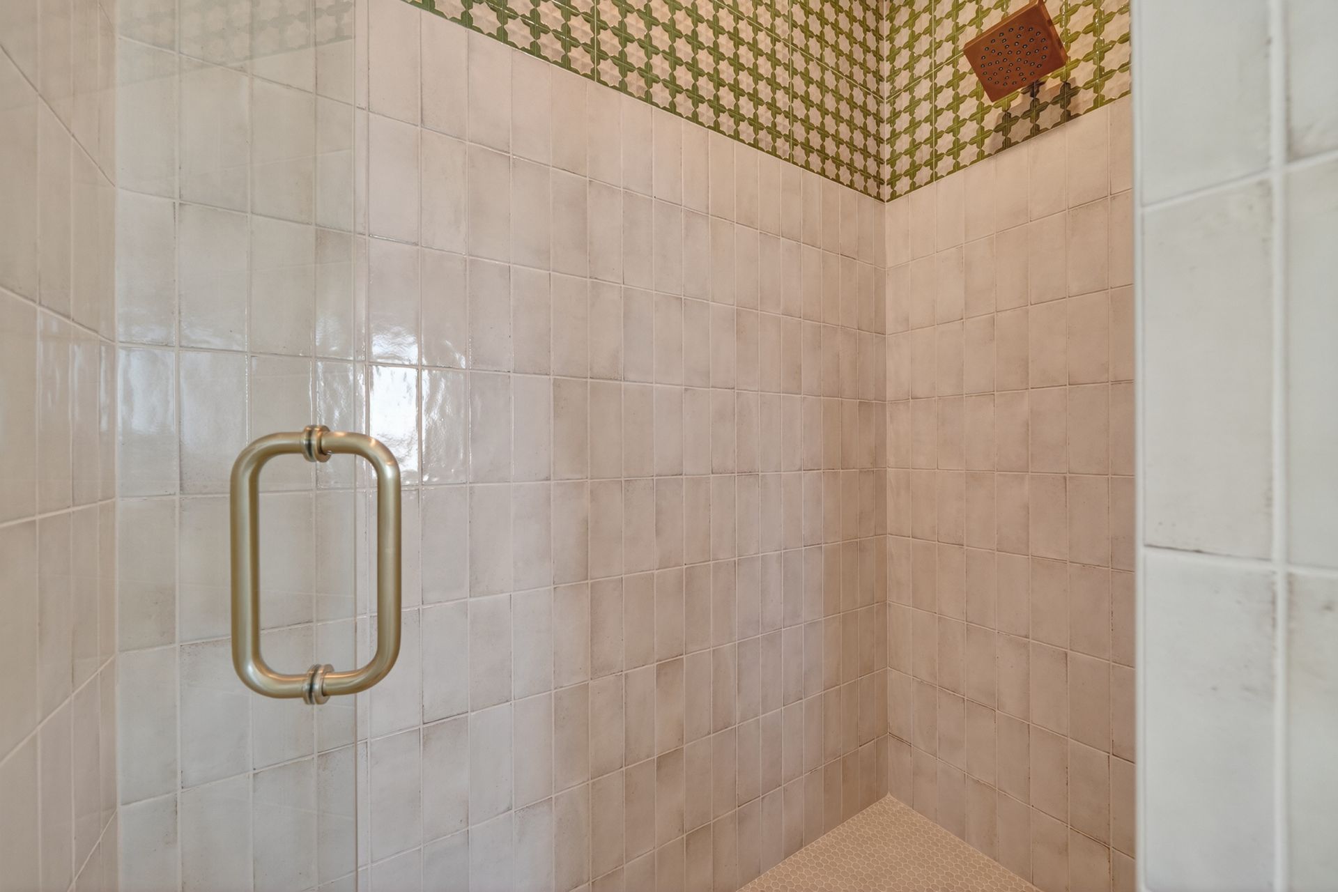 Tiled shower stall with brass handle and beige walls, viewed from the doorway
