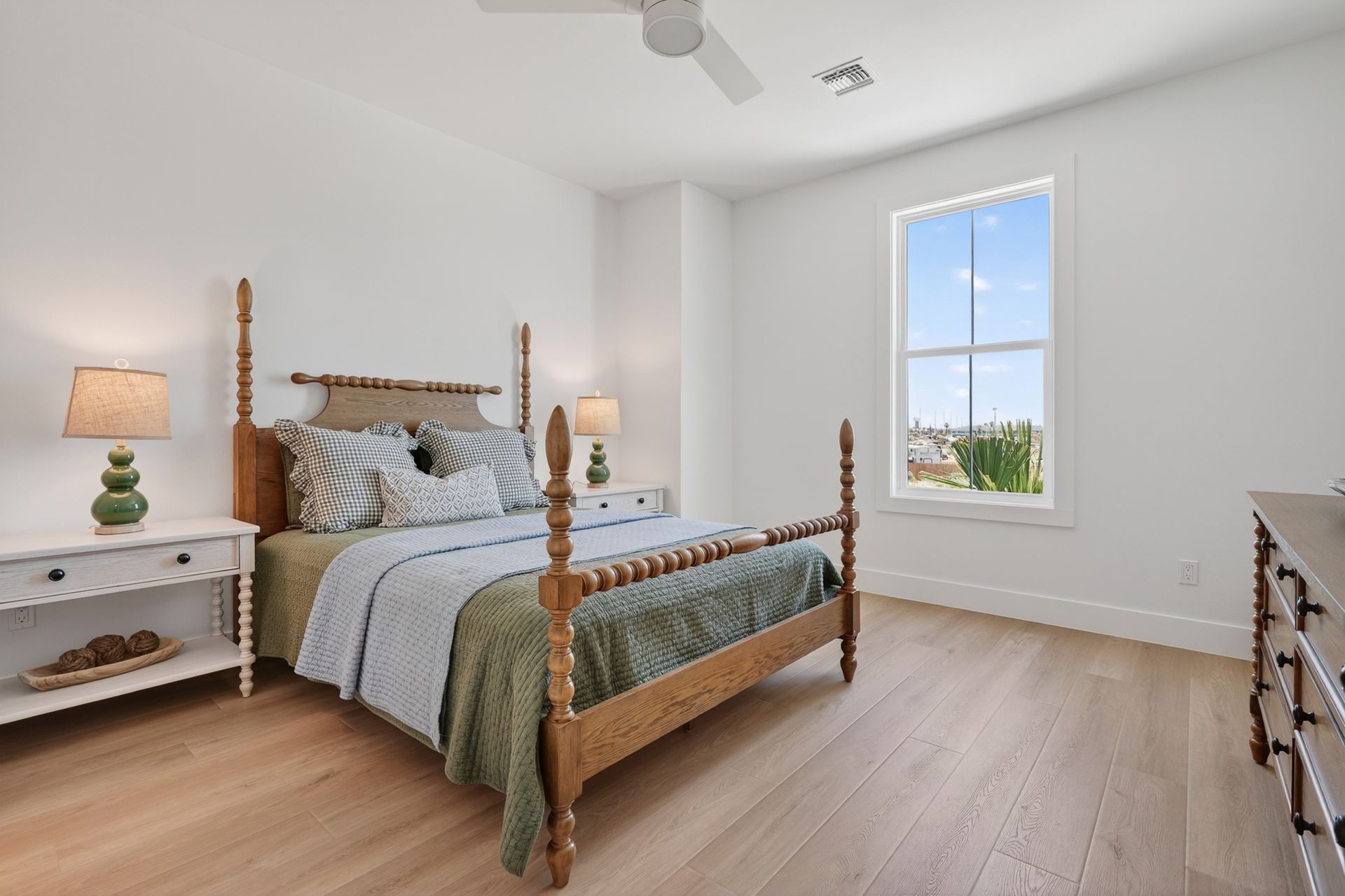 Bright bedroom with a wooden bed, two bedside lamps, and a large window with a city view.