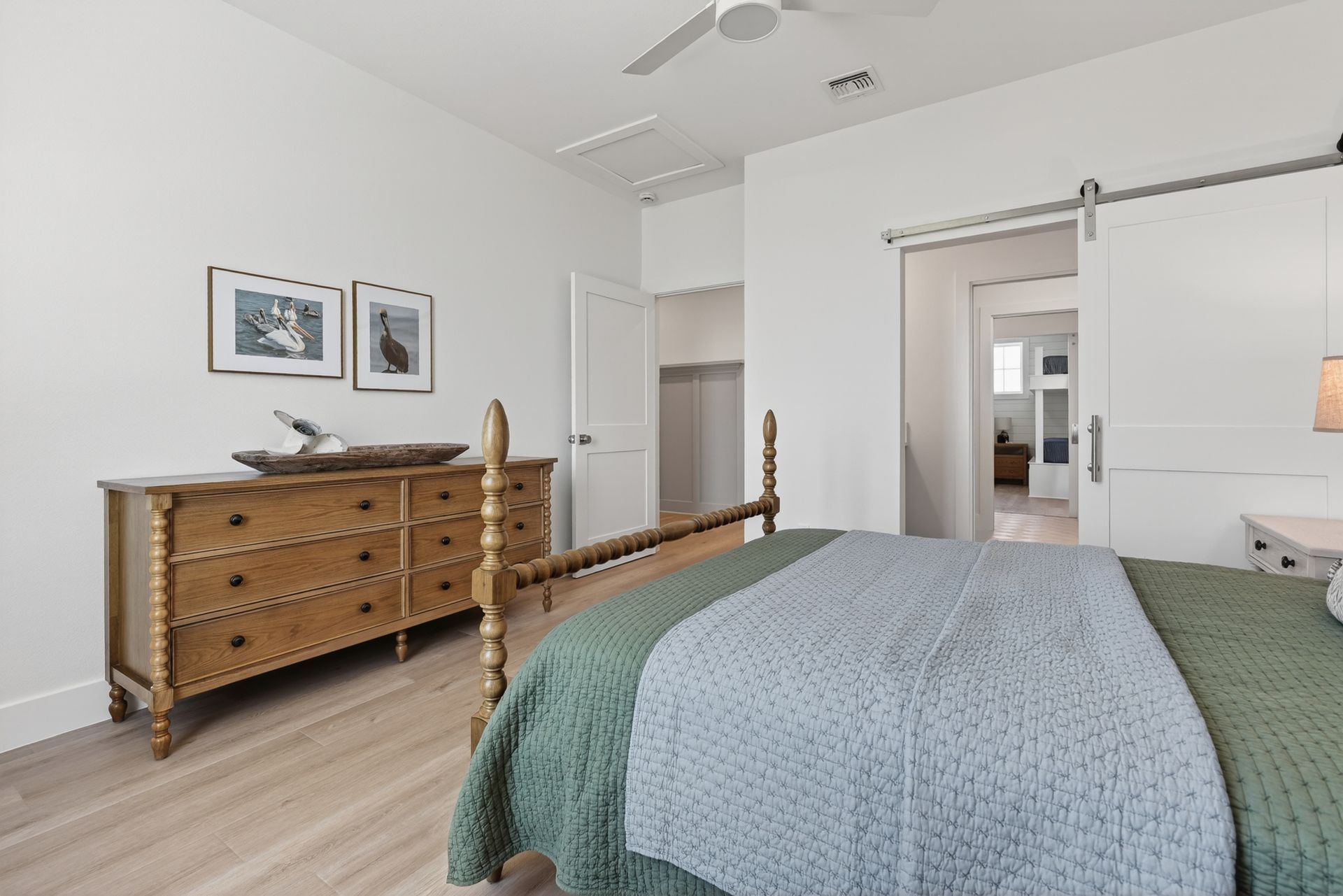 Bright bedroom with wooden dresser, bed, sliding barn door, and light gray decor
