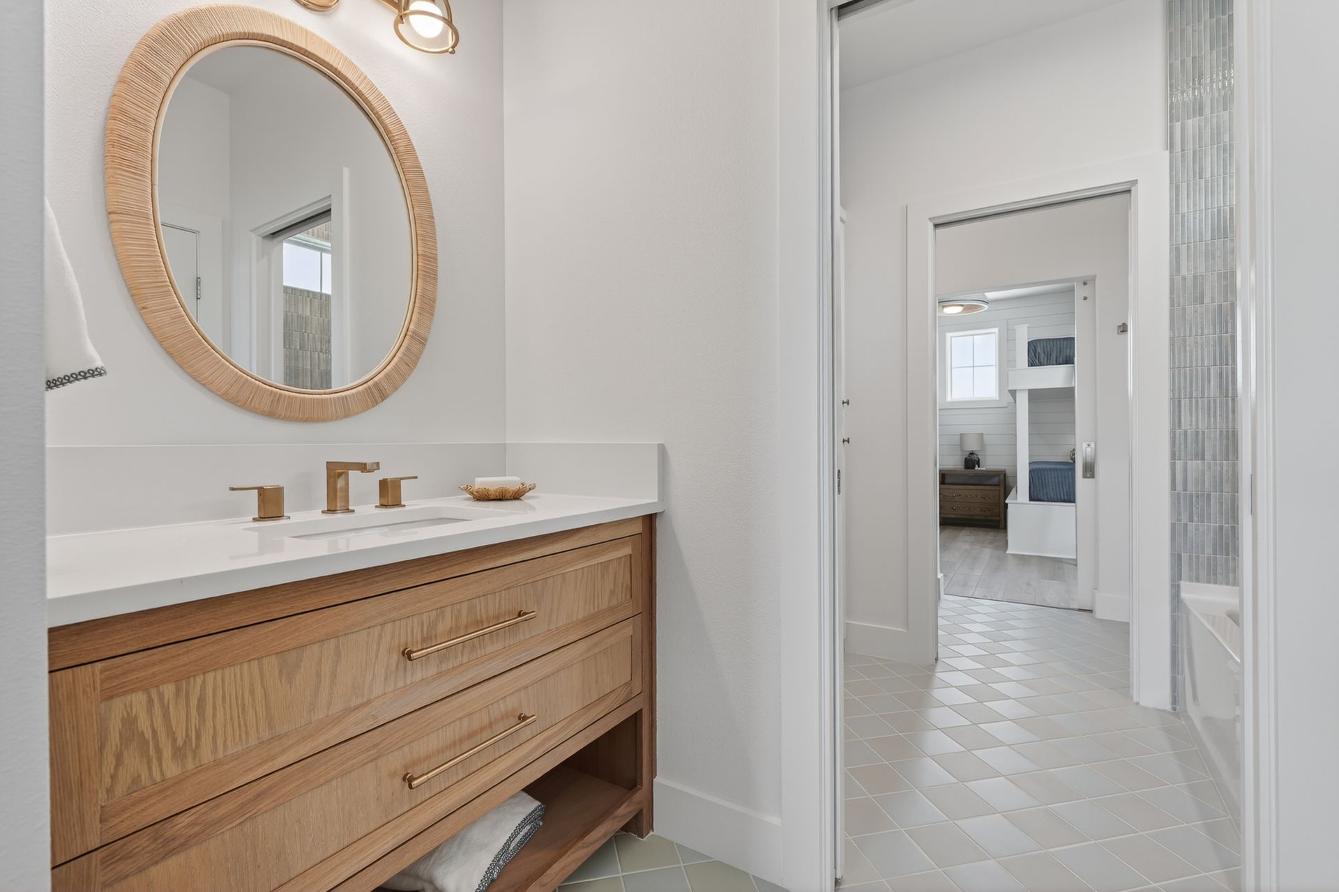 Bright bathroom with wood vanity, round mirror, and a hallway view into another room