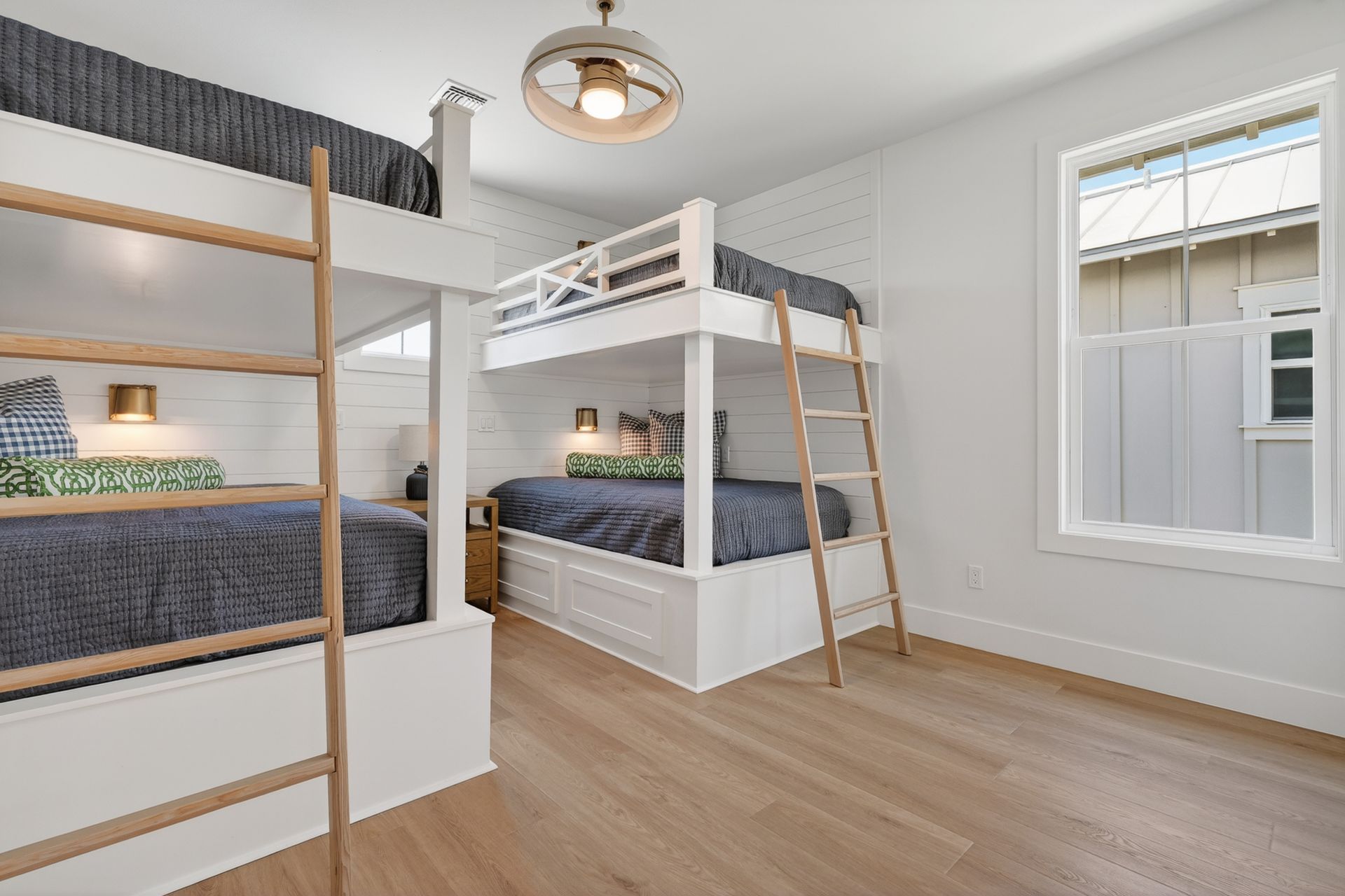 Bright bedroom with bunk beds, white walls, wood floors, and a window seat by two windows