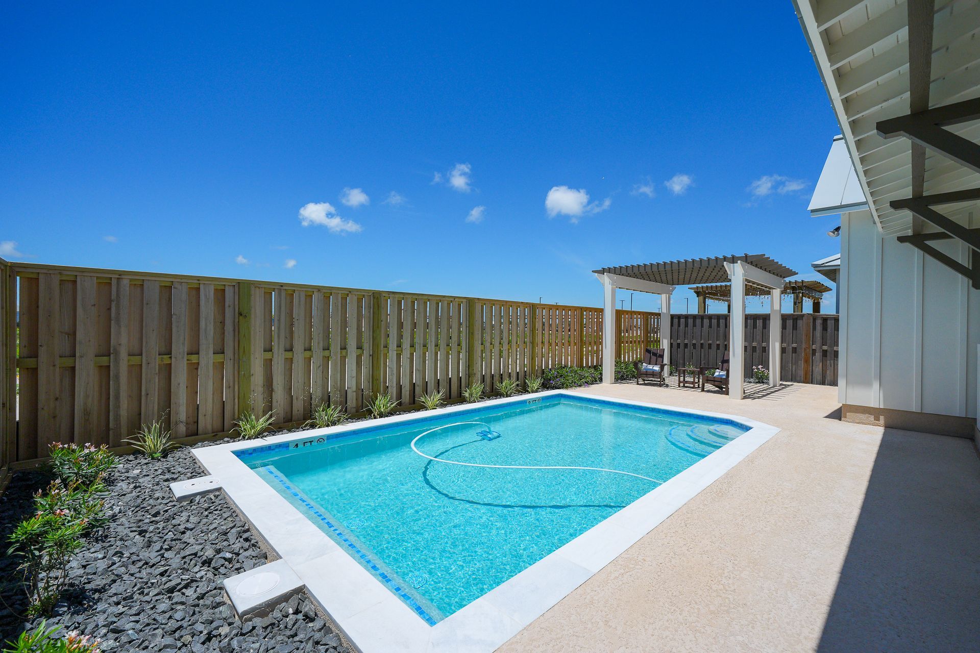 Backyard swimming pool beside a wooden fence under a bright blue sky