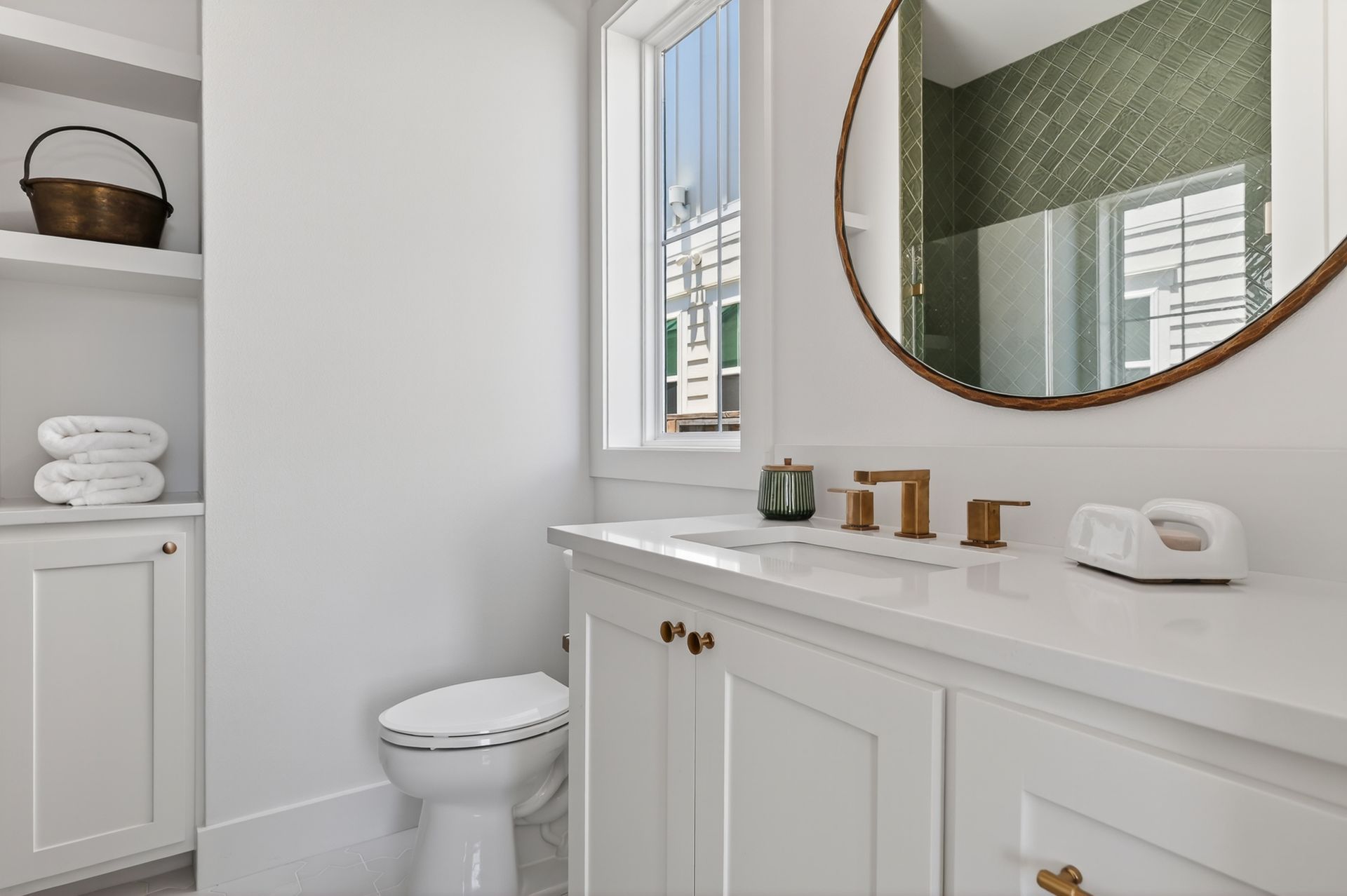 Bright white bathroom with vanity, round mirror, toilet, and green accent wall