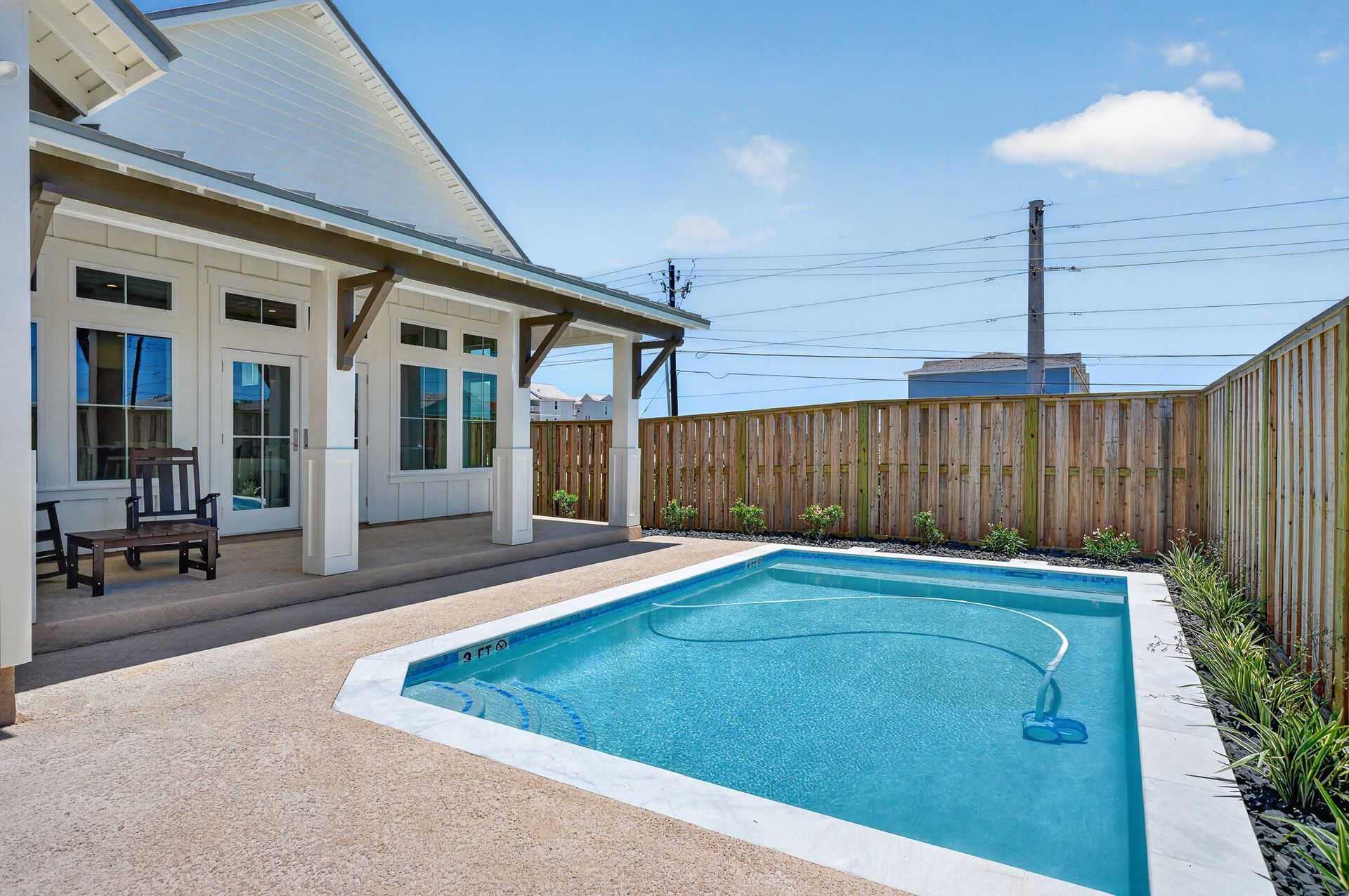 Backyard patio with a small blue swimming pool beside a white house and wooden fence